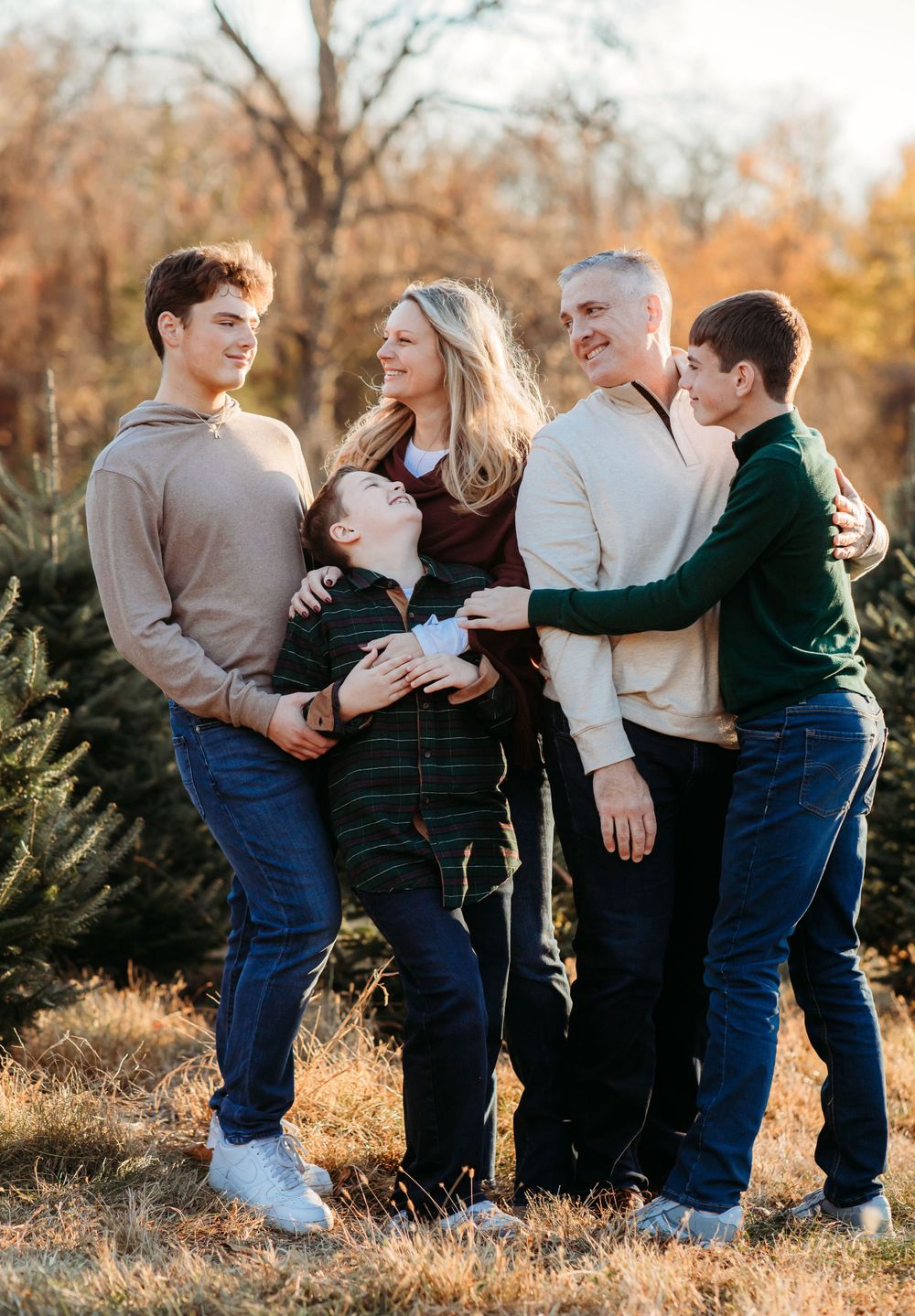 A family of five poses together outdoors at a Christmas tree farm during golden hour in autumn.