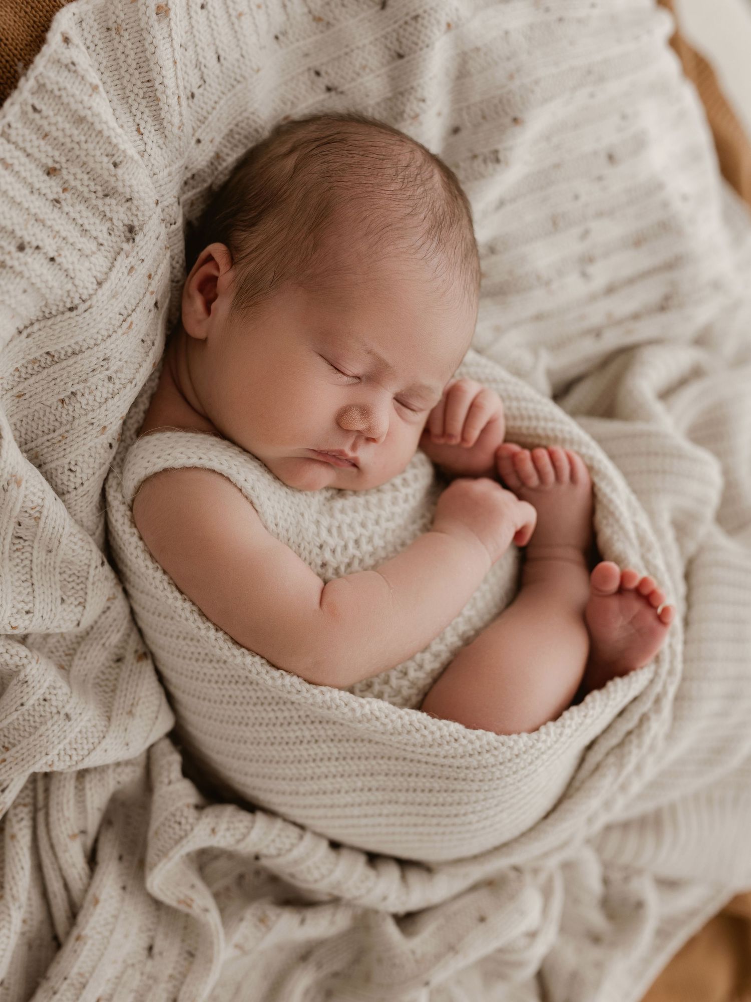 Peaceful sleeping newborn wrapped in cozy cream-colored knit blanket during professional photography session.