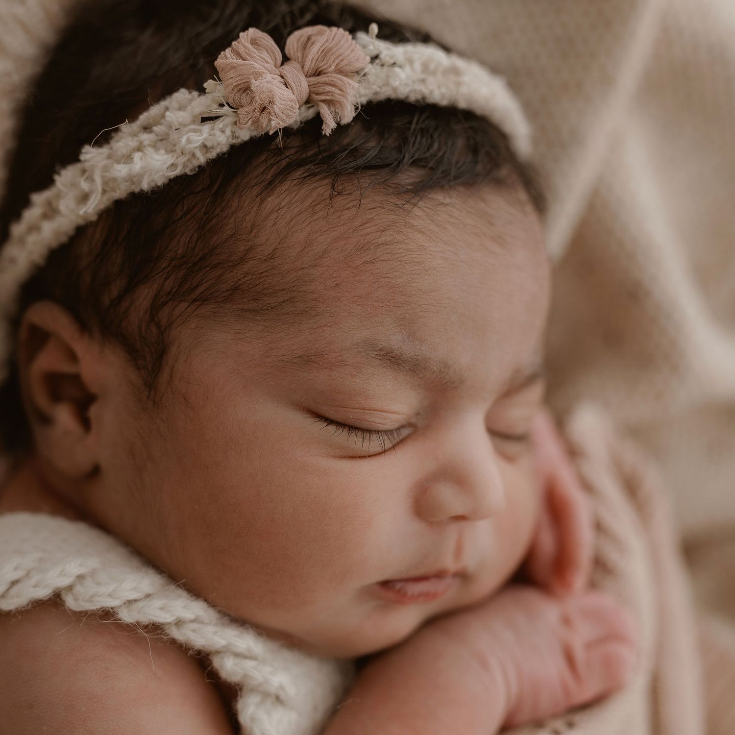 Peaceful sleeping newborn baby wearing delicate white lace headband in soft sepia tones.