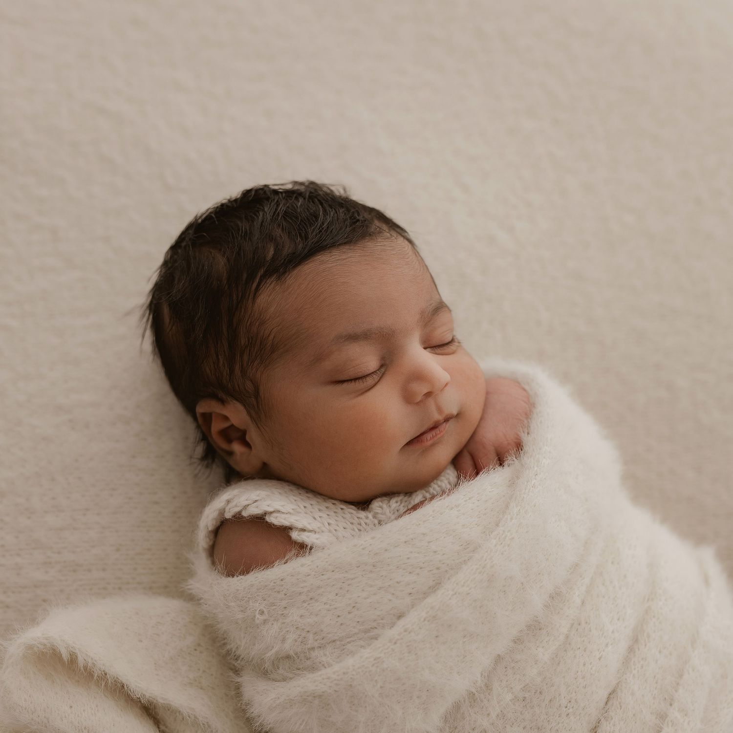 A sleeping newborn baby swaddled in soft white blankets shown in three peaceful poses against a neutral backdrop.