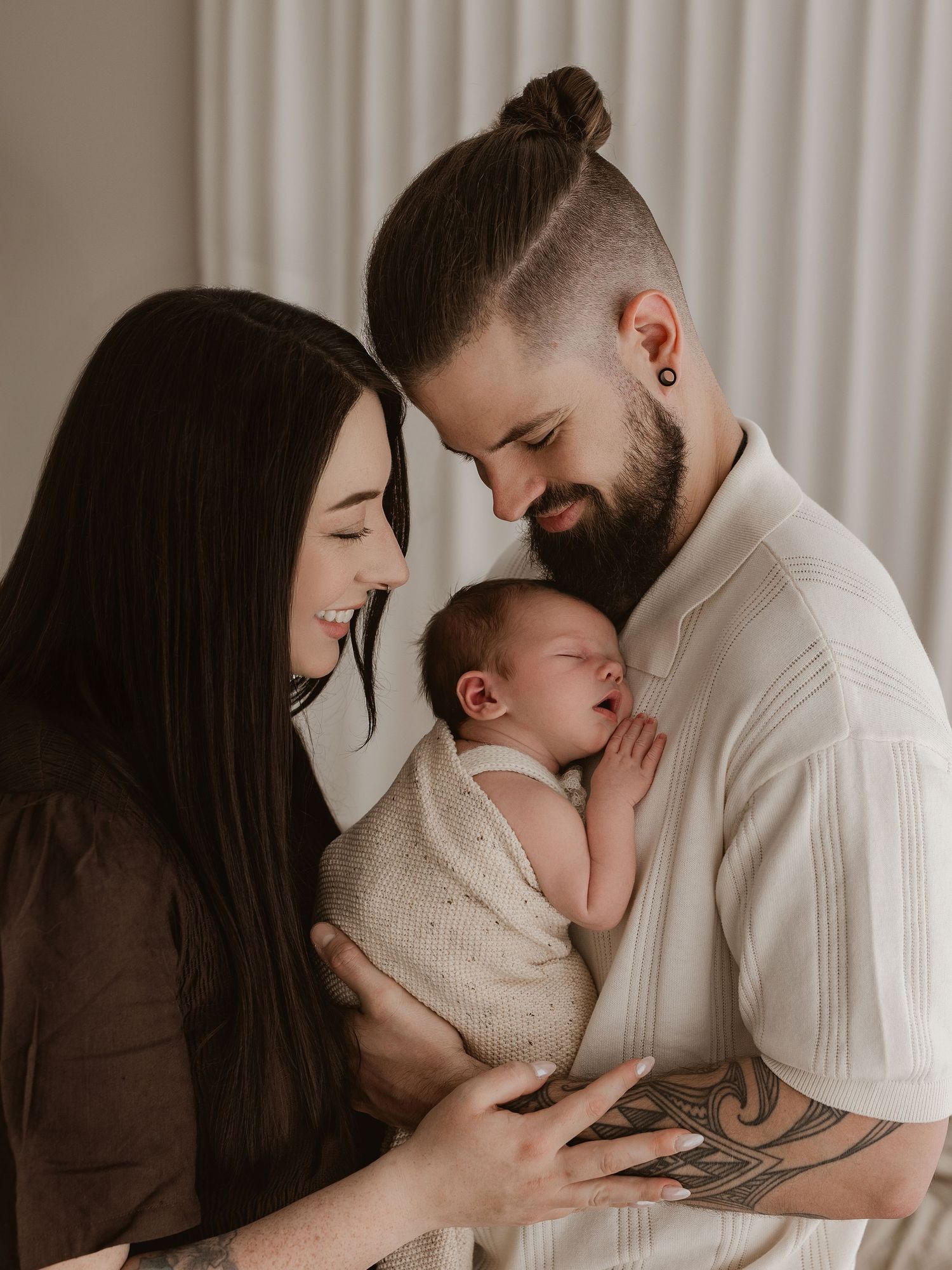 A tender family moment captured in black and white as parents share an intimate embrace with their newborn baby.