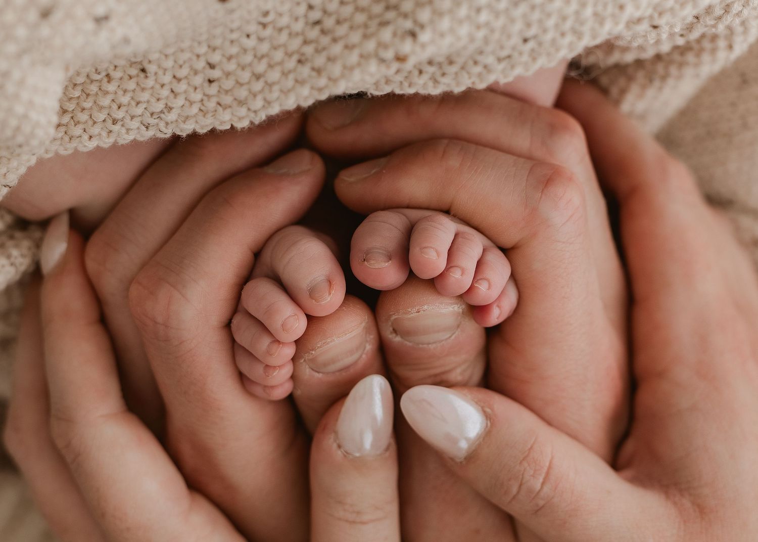 Close-up photo of tiny baby feet being gently held by adult hands with neutral nail polish.