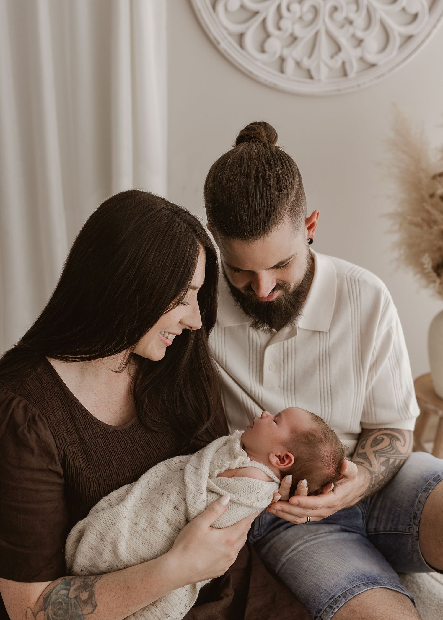 A series of intimate family moments showing parents bonding with their newborn baby in a minimalist setting with white decor.