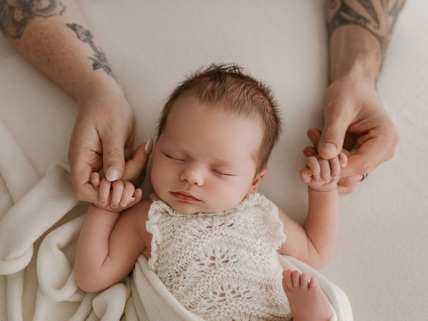 A sleeping newborn baby wearing a delicate lace romper is gently cradled during a professional photography session.