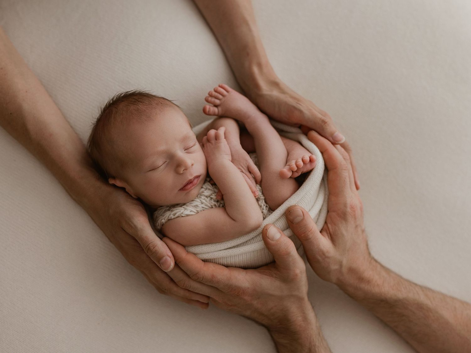 A series of artistic black and white photographs showing gentle hands cradling a sleeping newborn baby.