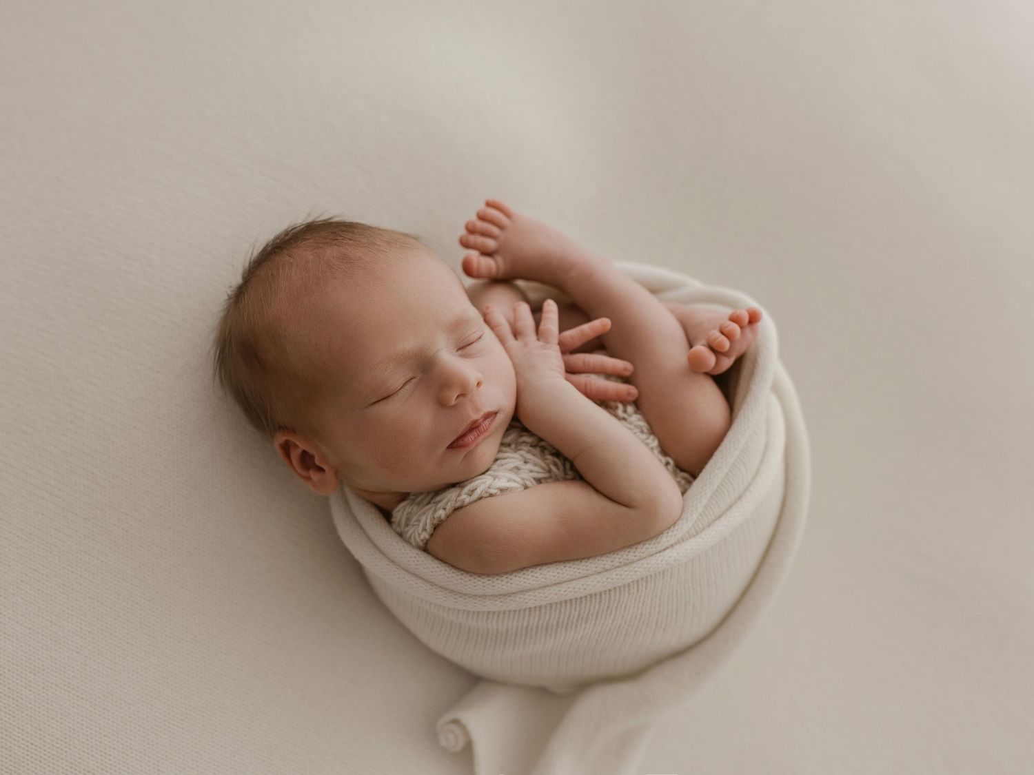 A series of black and white photographs showing a sleeping newborn baby wrapped in soft white fabric.