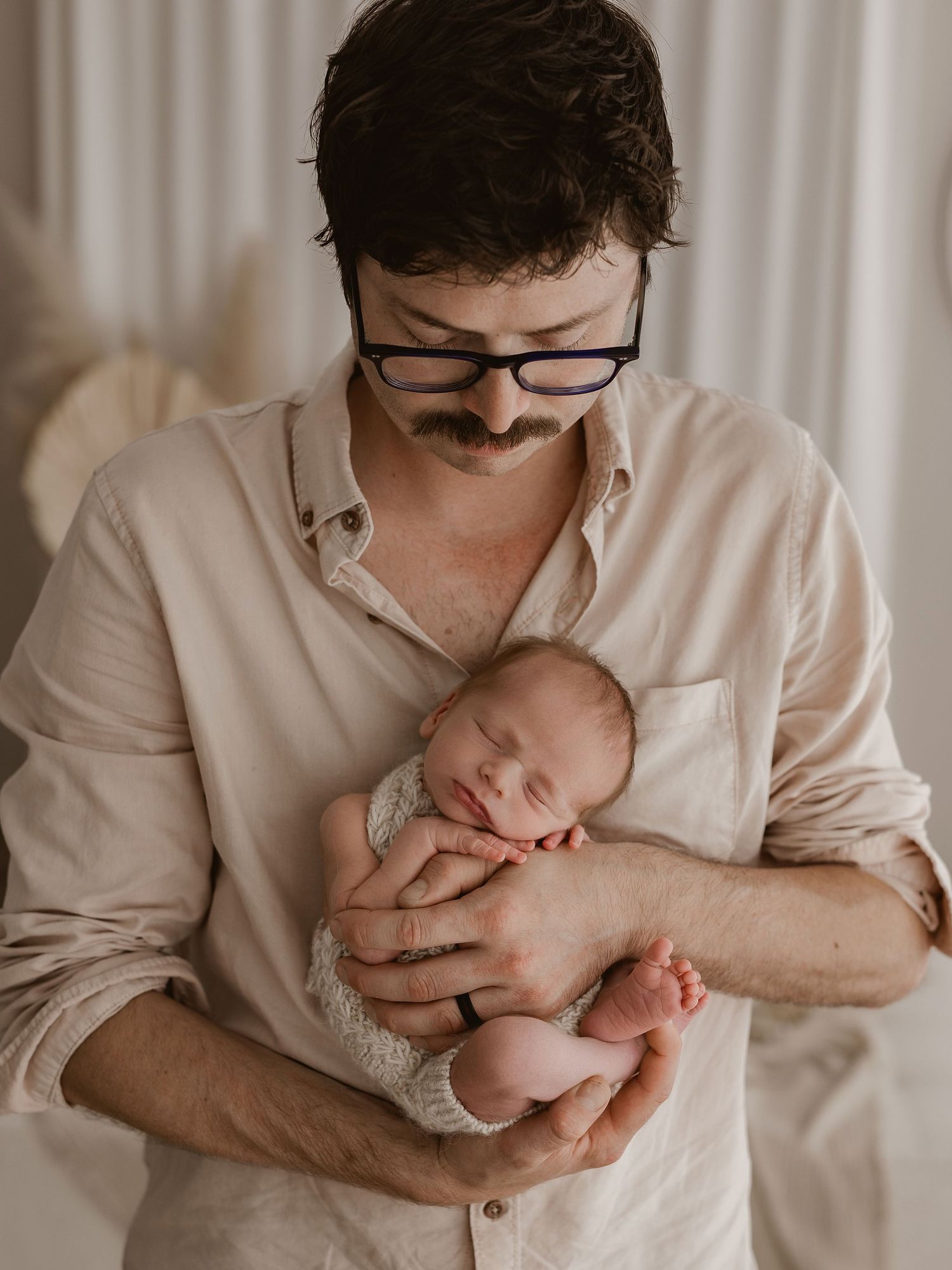 A parent in a white shirt holds and kisses their newborn baby in a series of tender black and white photographs.