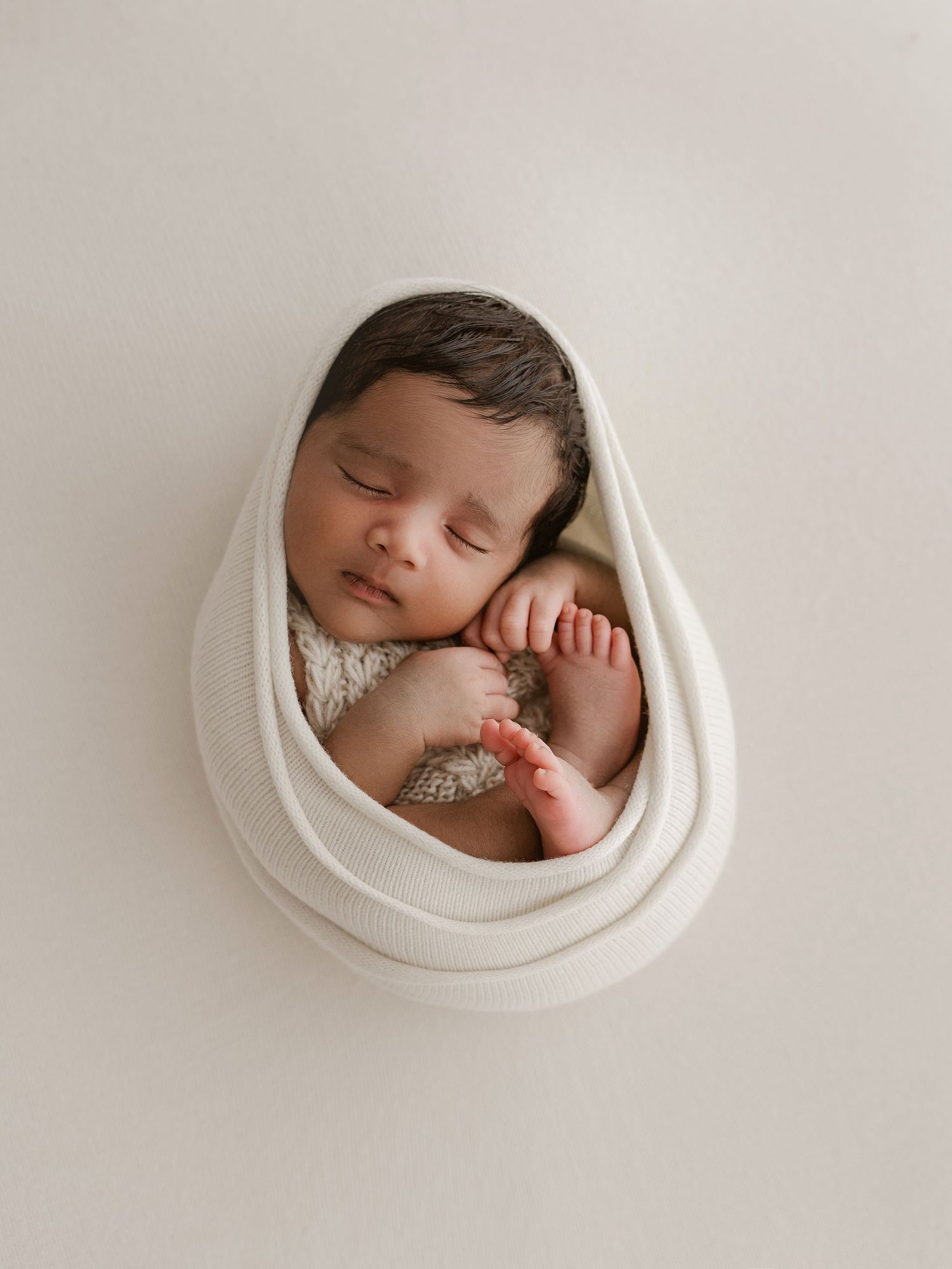 A sleeping newborn baby swaddled in white fabric shown from different angles in a series of four connected photos.