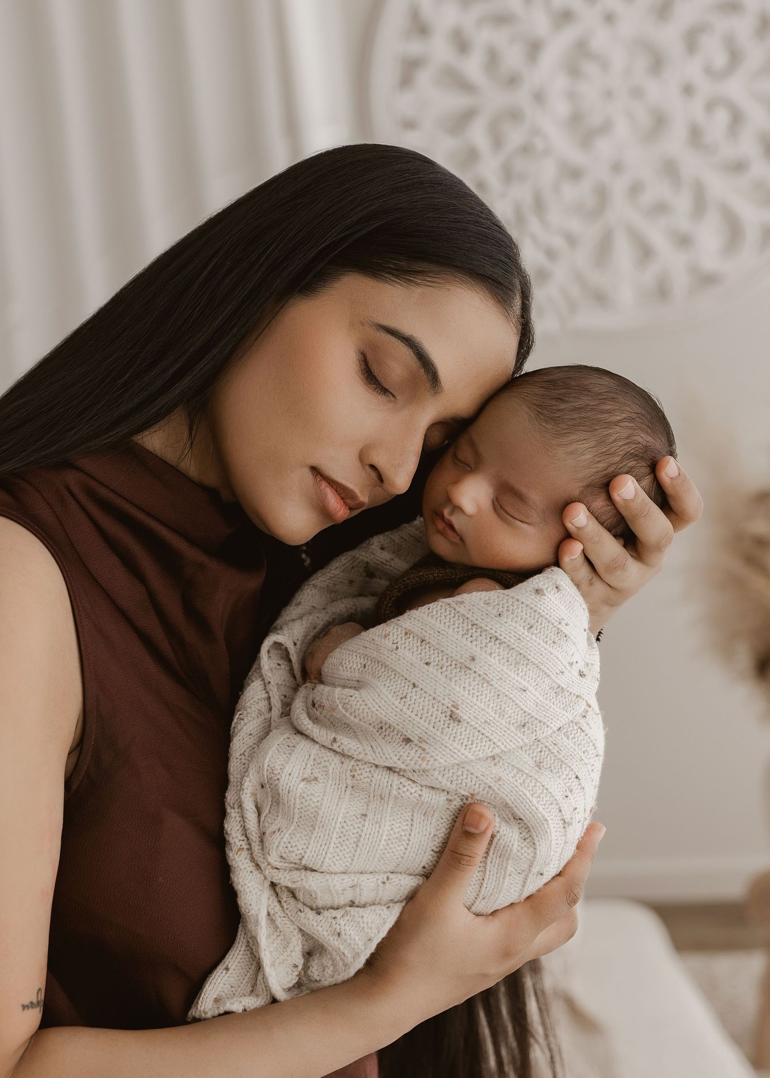 A tender moment captured in soft light showing a parent cradling a newborn baby wrapped in a white knit blanket.