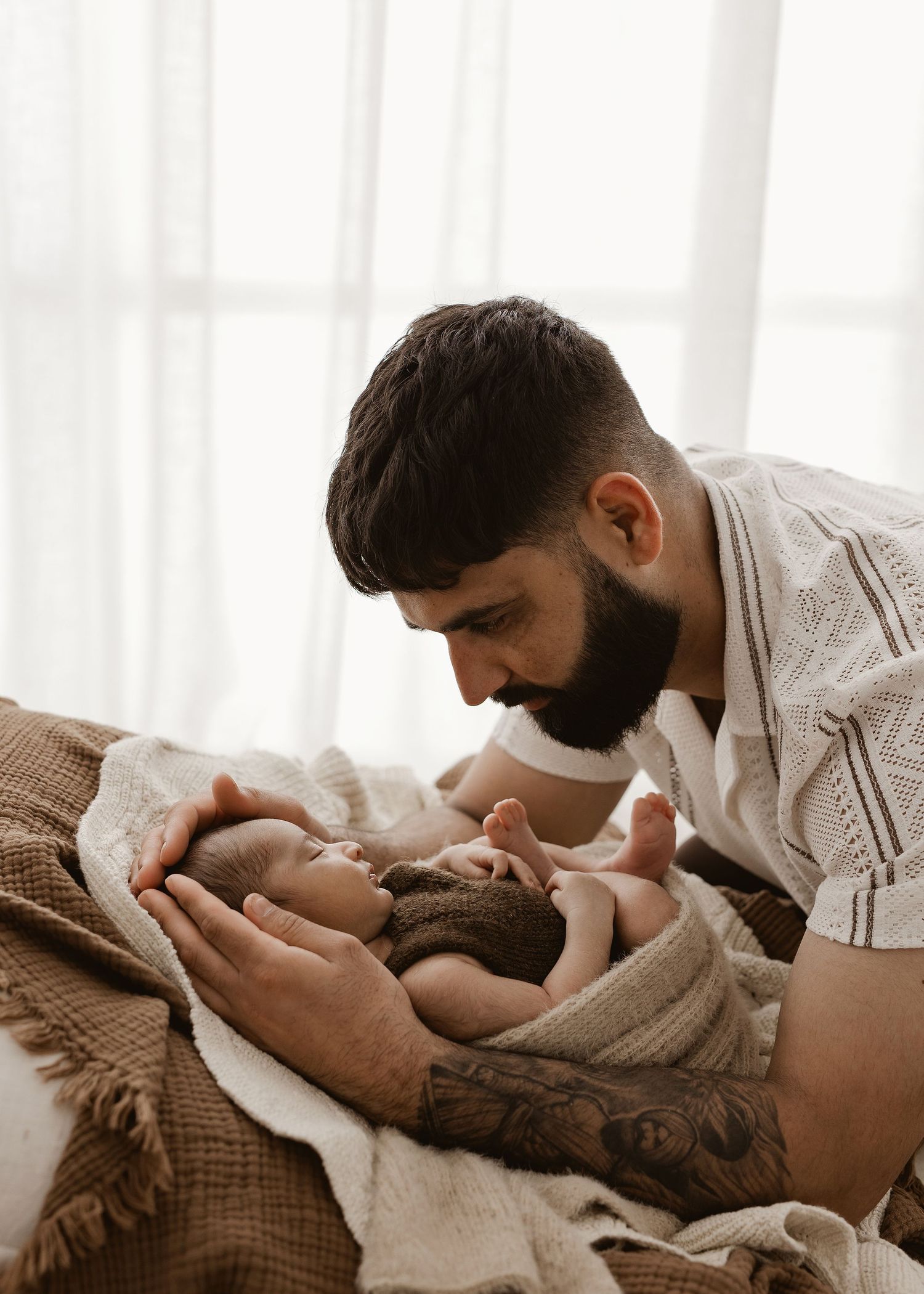 A tender moment between parent and newborn baby lying together on a bed in a bright room.
