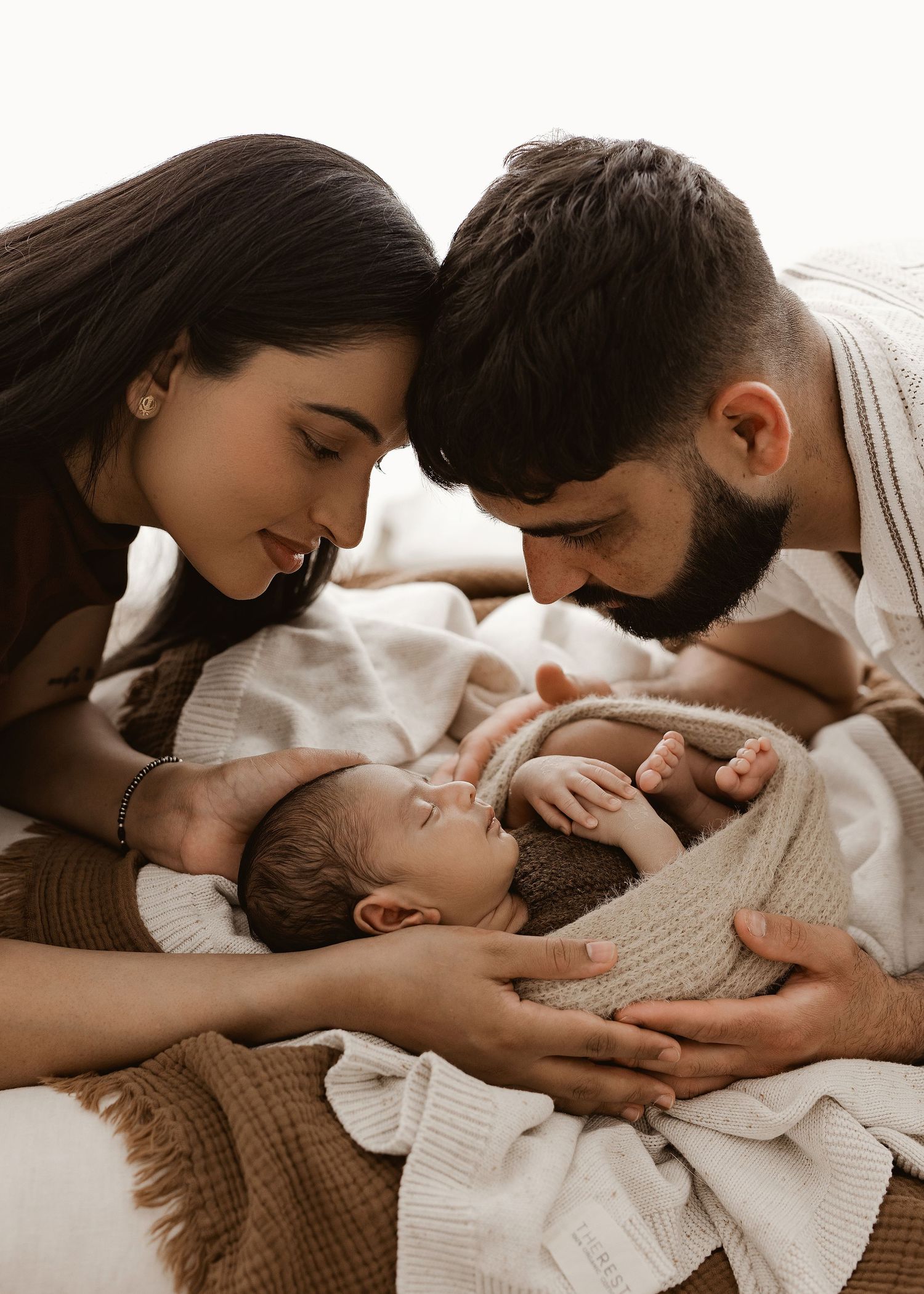 Parents share tender moments with their baby while laying on a white bed together.