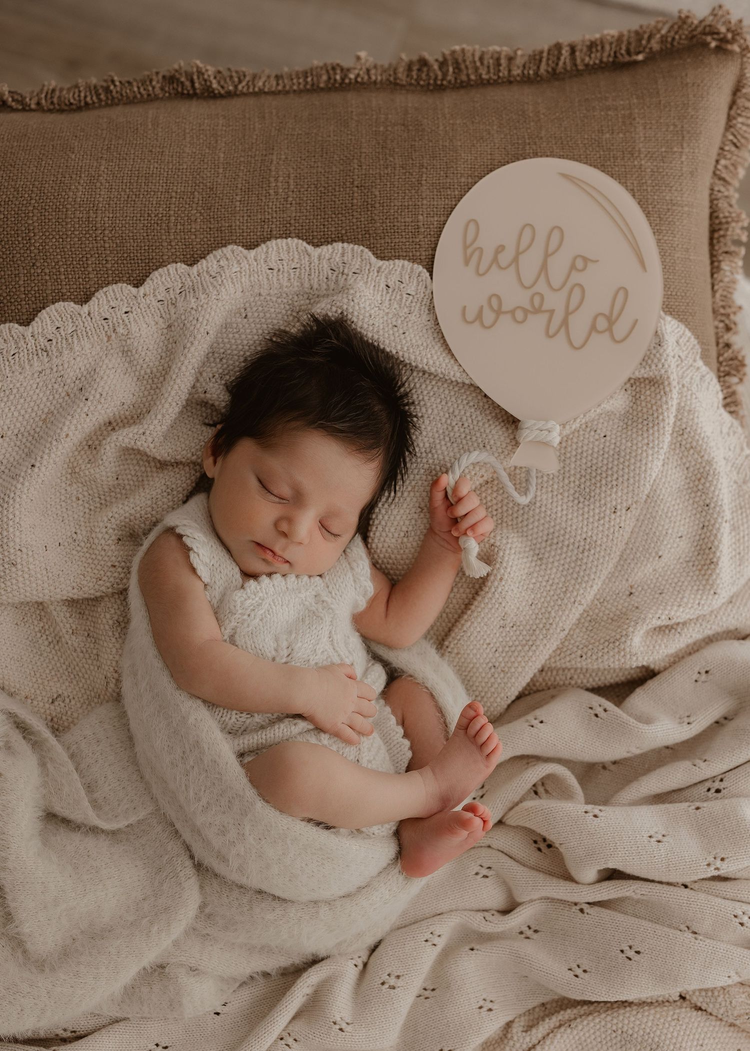 A sleeping newborn baby in white swaddle blanket with 'hello world' text overlay on beige background.