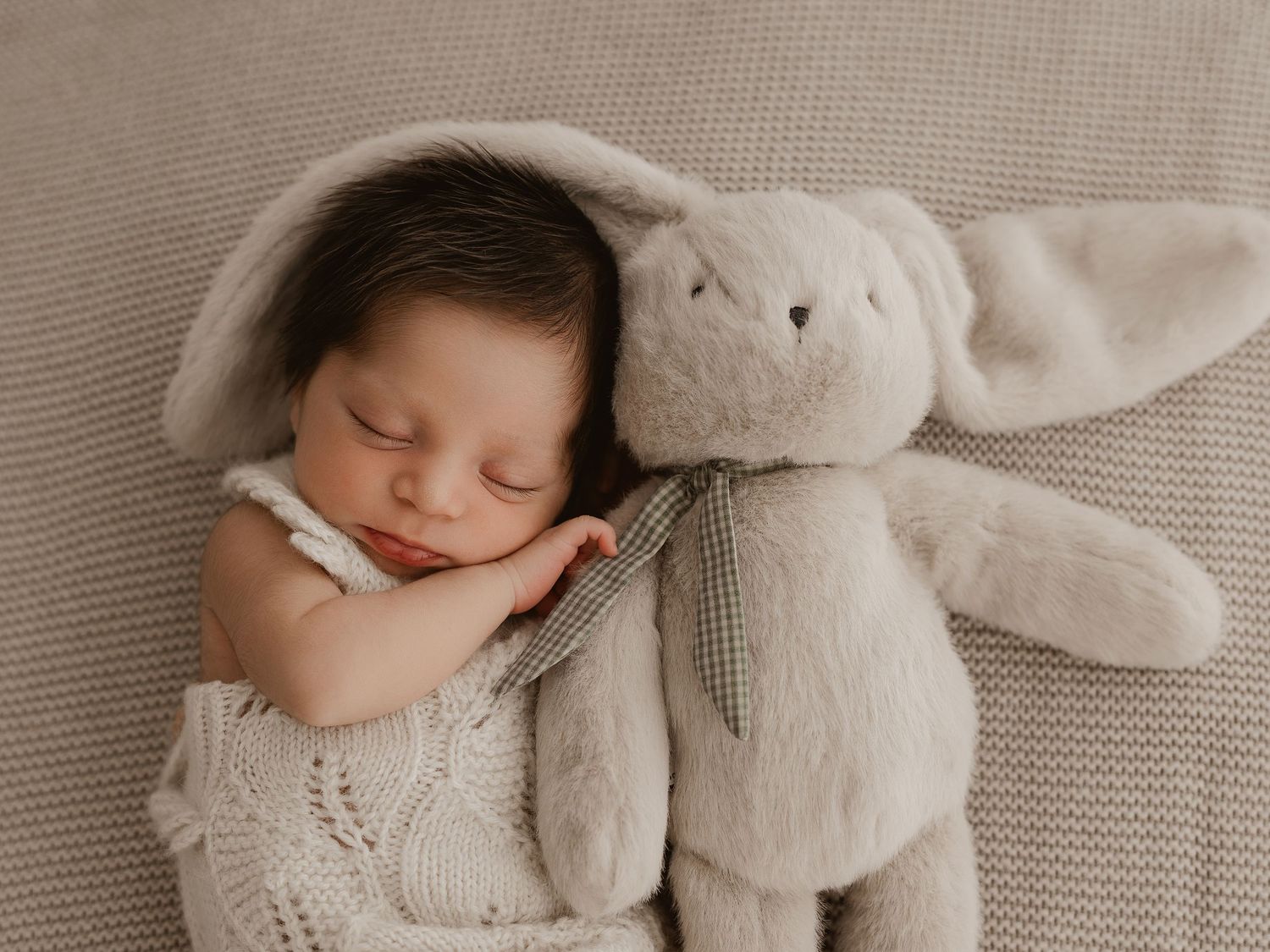 Sleeping baby wrapped in cozy knit blanket with plush bunny toy.