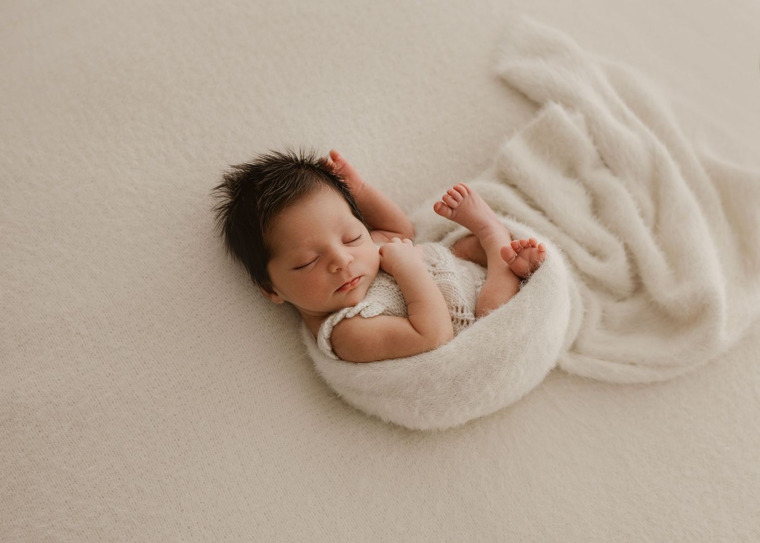 Newborn baby sleeps peacefully wrapped in soft beige blankets during professional photography session.