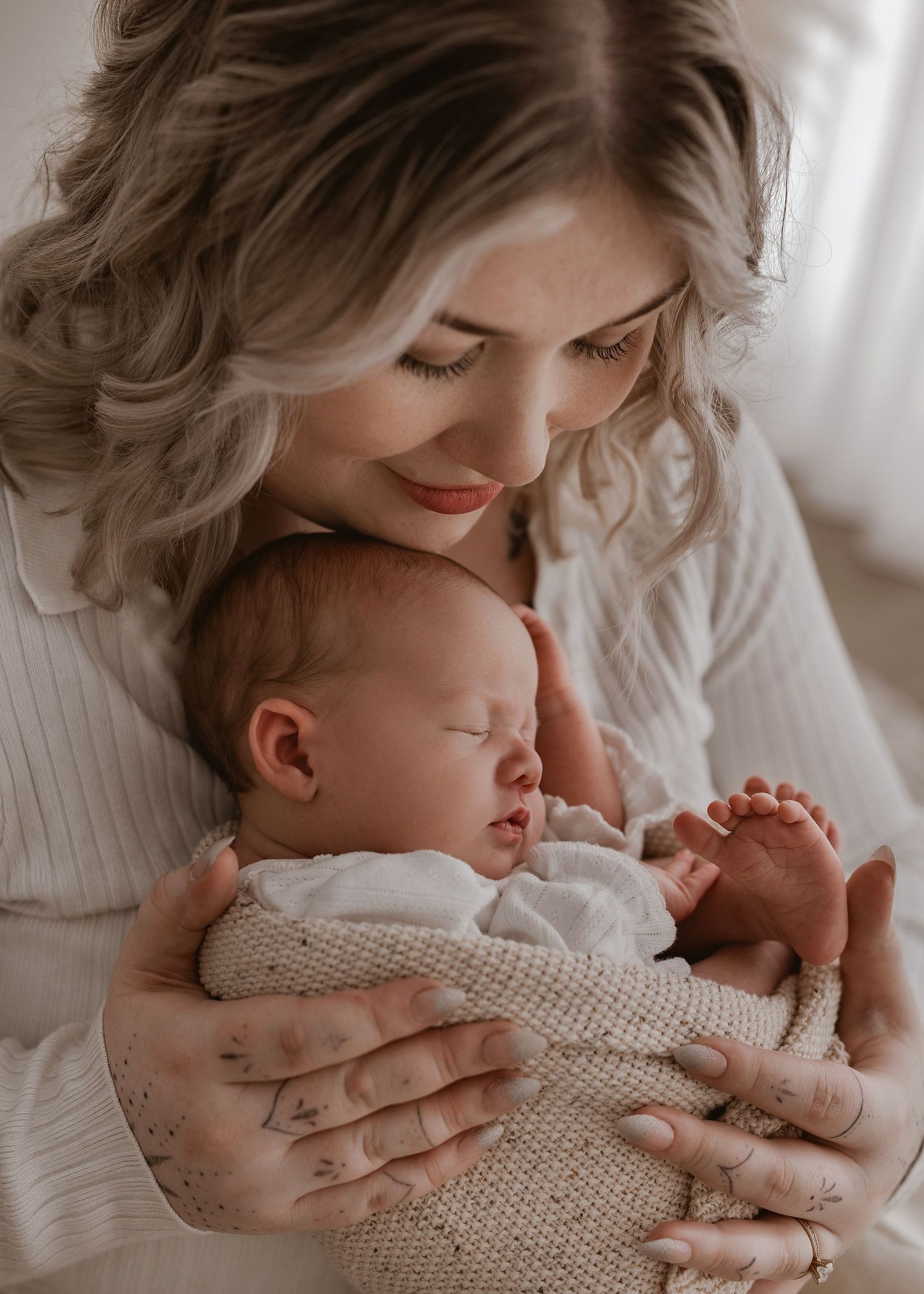 Tender moment of parent cradling sleeping newborn baby wrapped in soft knit blanket in natural window light.