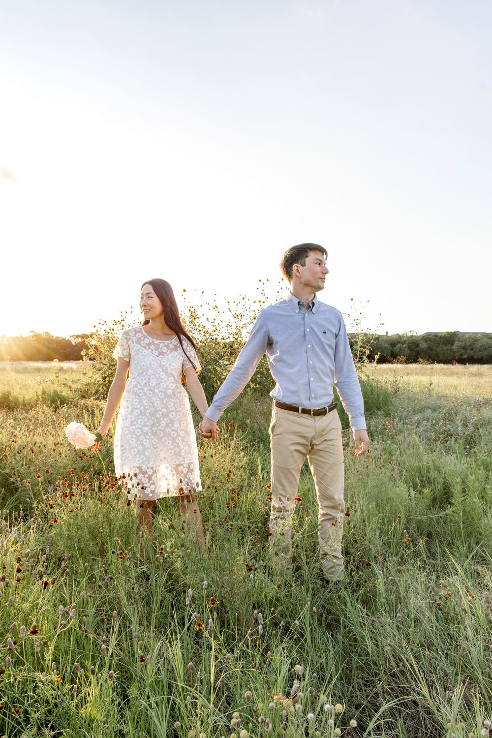 Couple walking together through a sunlit wildflower meadow at golden hour.