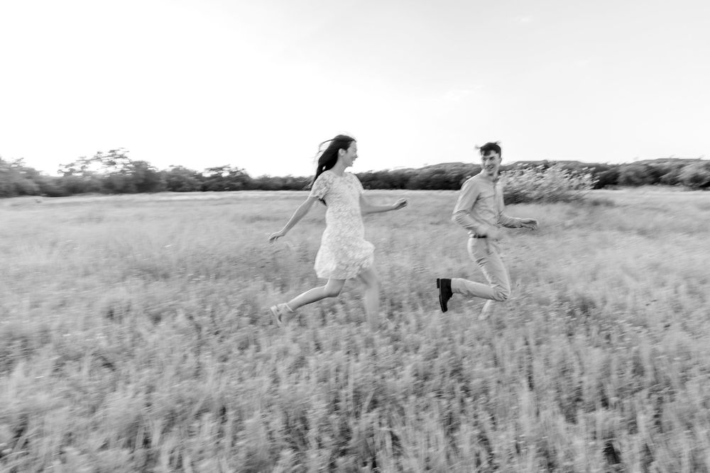 Black and white photos capture joyful moments of people running and dancing through a wheat field on a summer day.