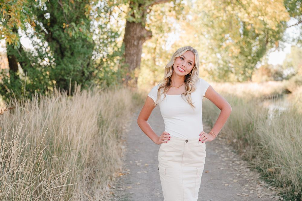 Elegant white dress portrait taken on a nature path with tall grass and trees in warm sunset lighting.