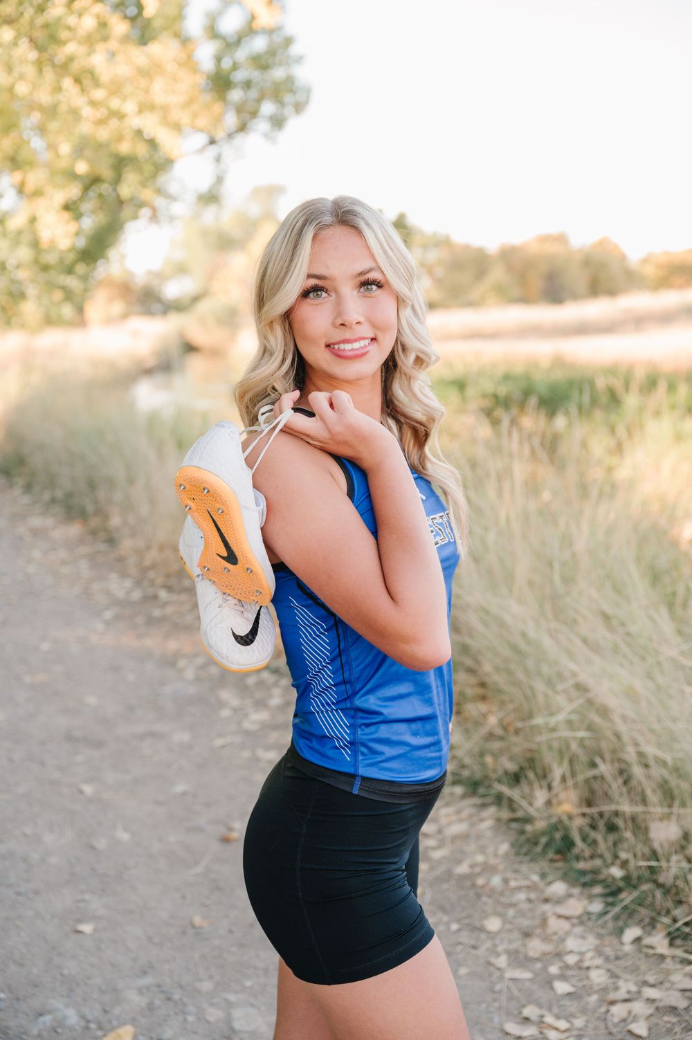 An athletic portrait featuring a blue tank top and workout attire on a sunlit dirt path with golden grasses.