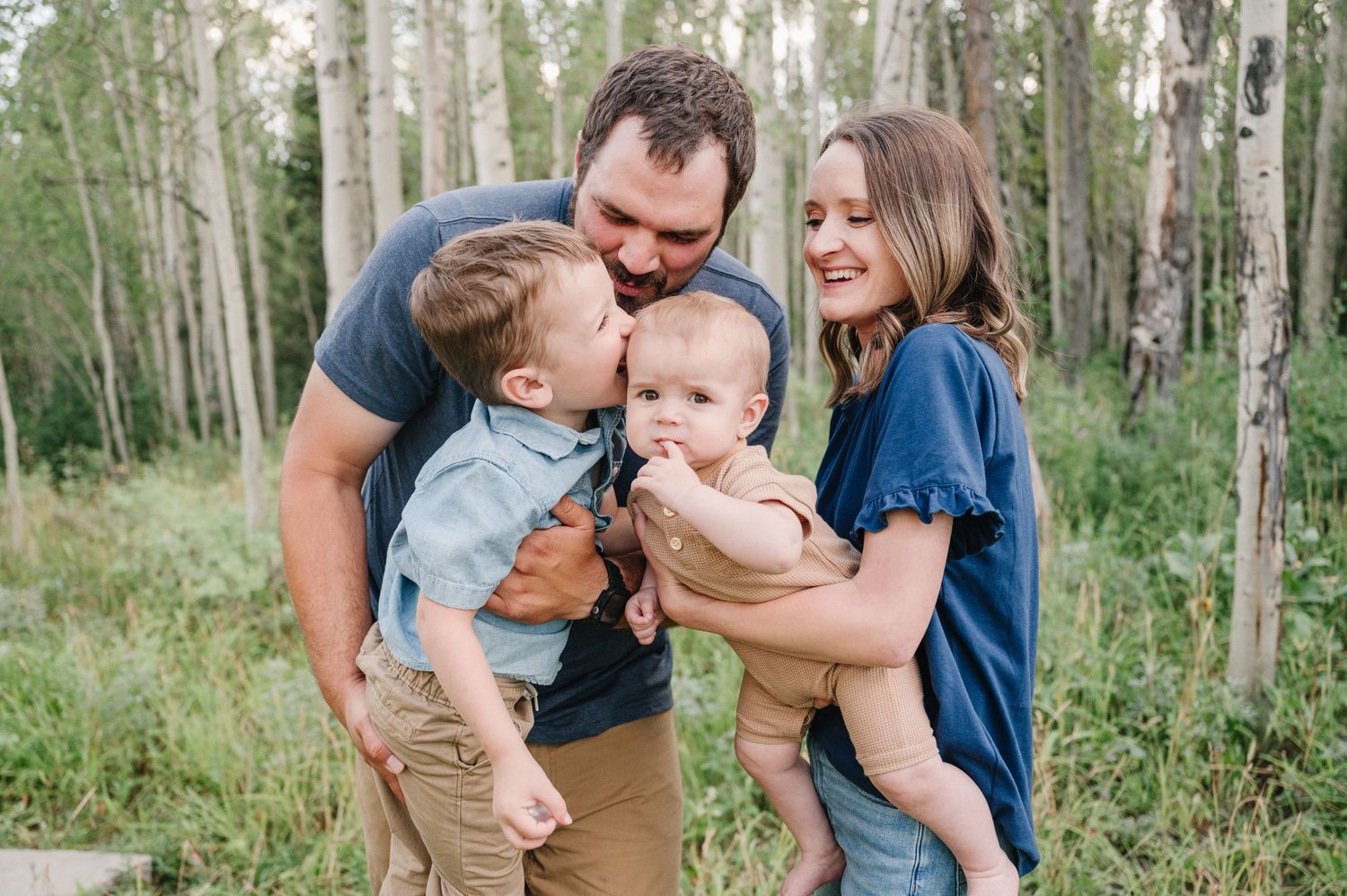 A family enjoying a tender moment together while standing in a peaceful aspen forest grove.