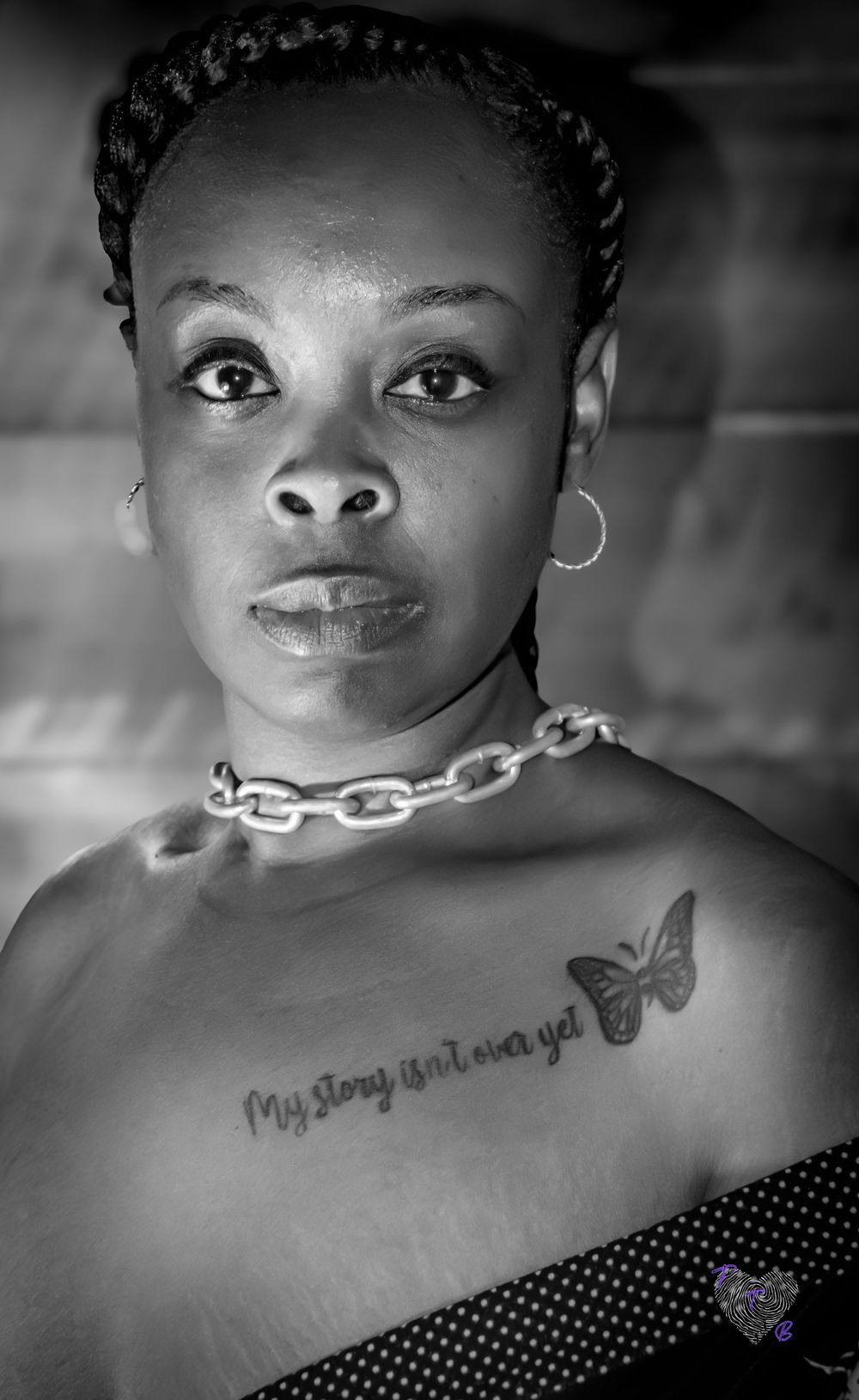 Black and white portrait of a woman with braids, chain necklace, and butterfly tattoo reading My story isn't over yet.