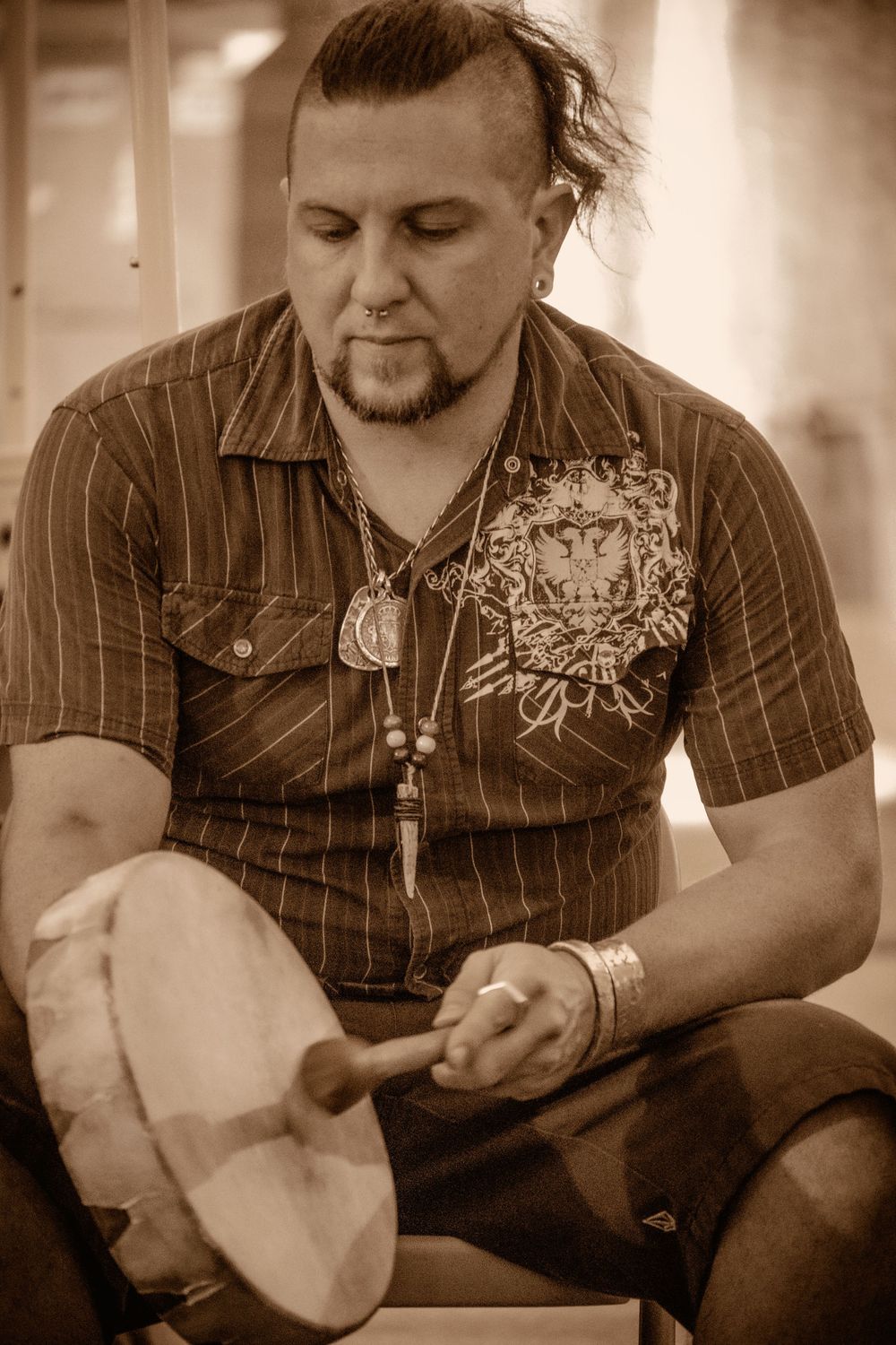 Sepia toned photo of someone in a striped shirt with decorative design wearing necklaces and sitting down.