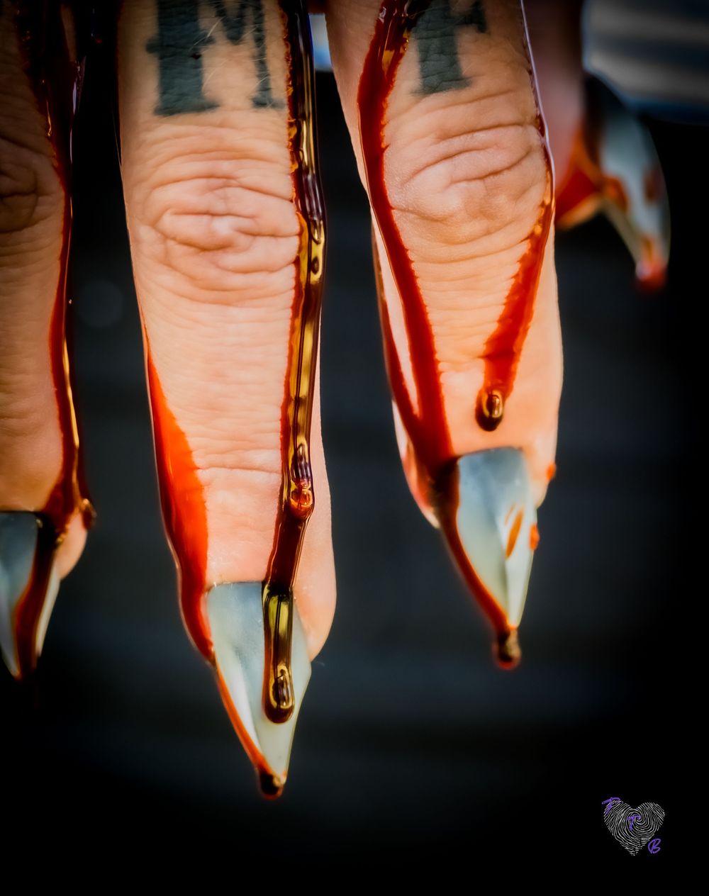 Close-up of fingers with tattoos dripping with red liquid over sharp pointed nails in dramatic lighting.
