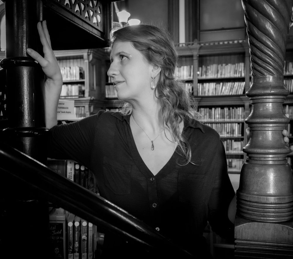 A black and white photo showing someone looking up inside an ornate Victorian library with elegant columns.