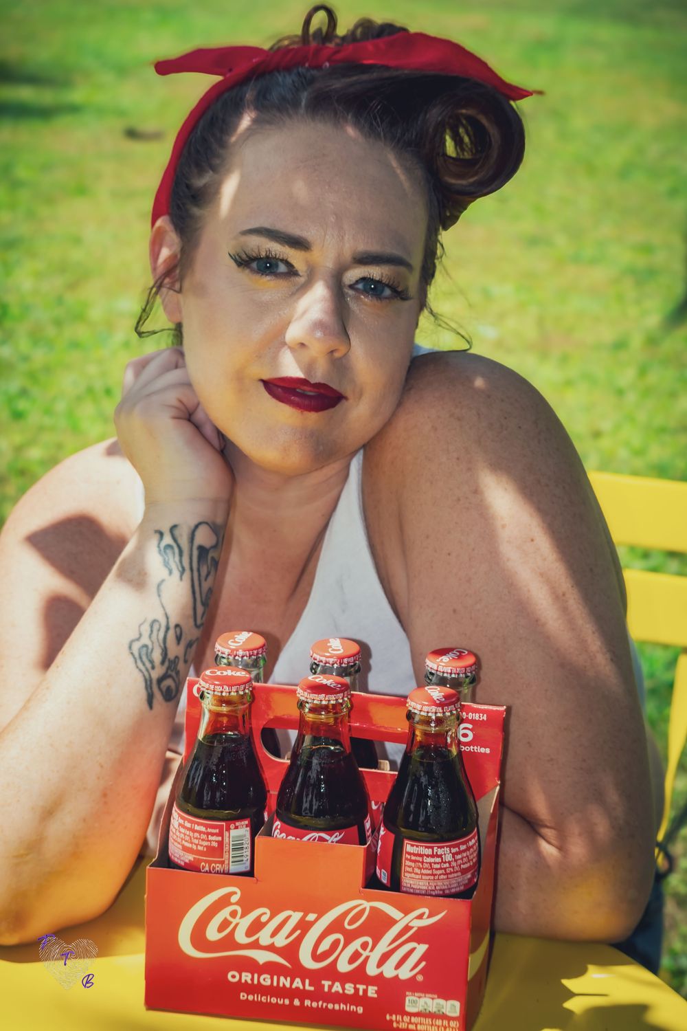 Woman with red headband poses outdoors with Coca-Cola Original Taste six-pack bottles on yellow table.