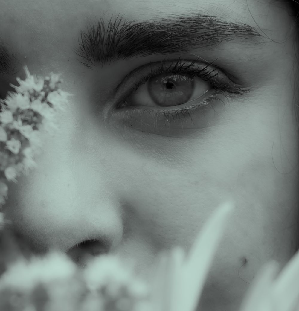 A dramatic black and white close-up photograph of an eye with flowers framing the composition.