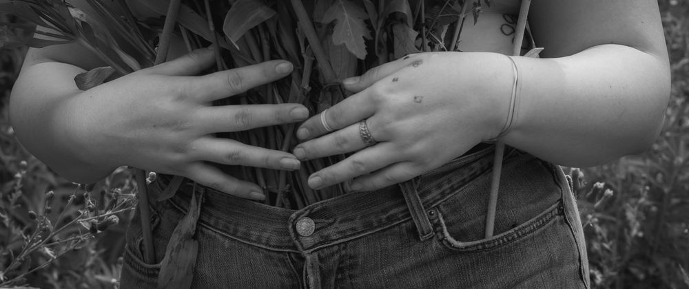 Hands with wedding rings resting together in a celebratory pose against green outdoor foliage.