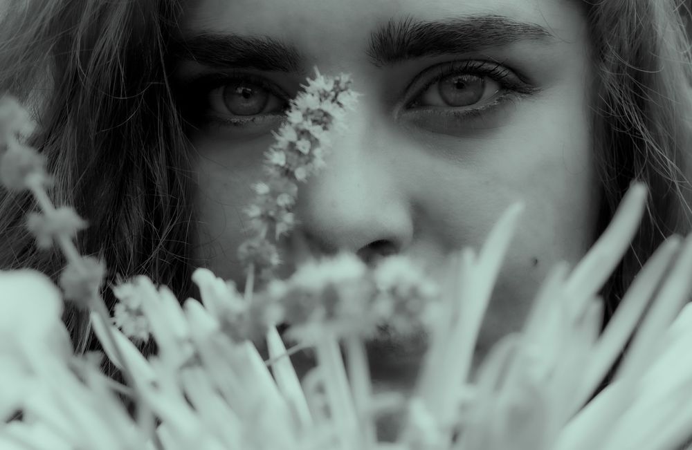 Close-up black and white view showing eyes peering through delicate white ferns and floral elements.