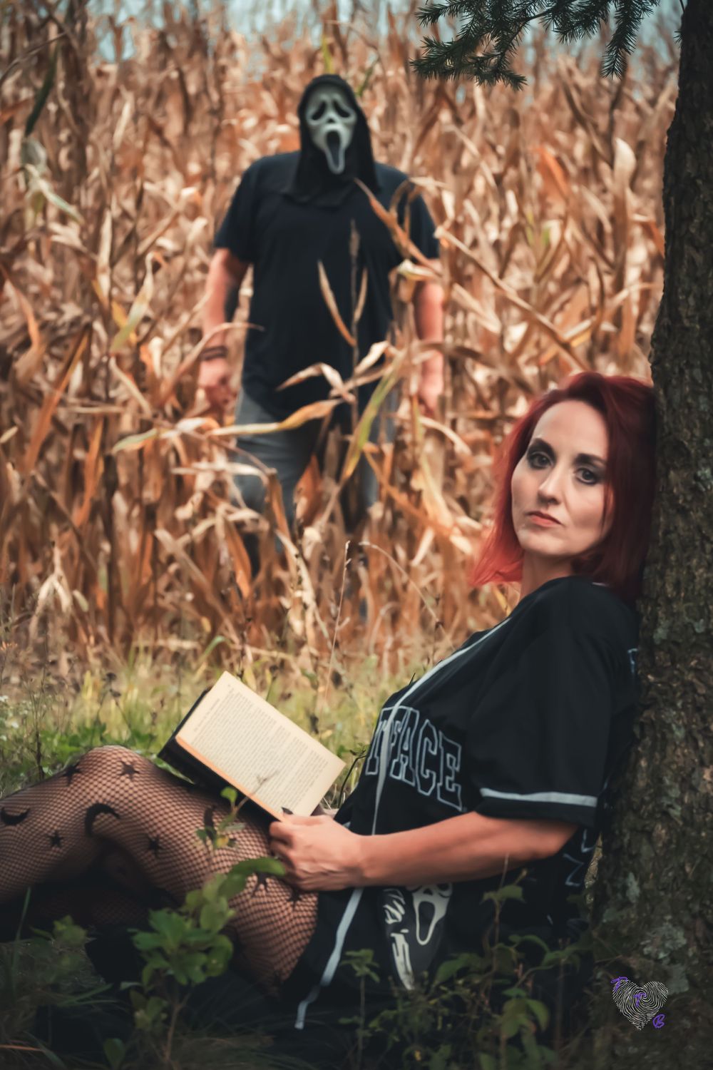 A red-haired woman reads a book by a tree while a person in a Ghostface mask lurks in a cornfield behind her.