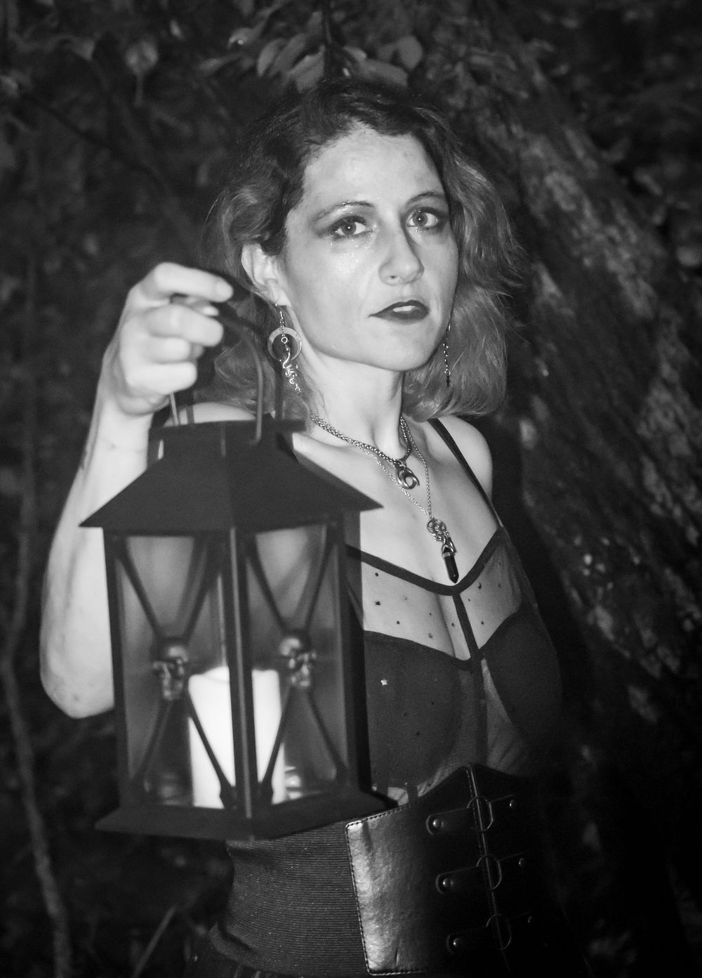 Black and white photograph showing a spooky gothic scene with a person holding a vintage lantern in dark atmospheric lighting.