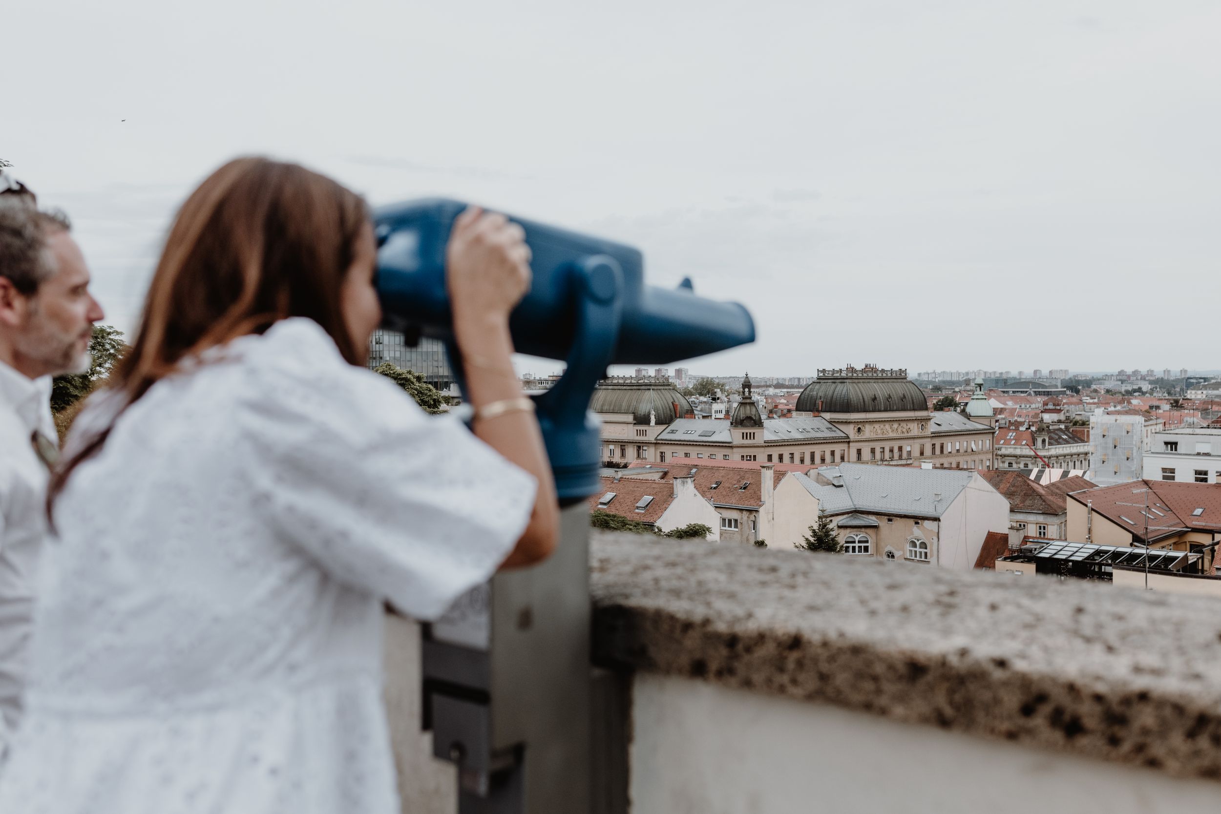 Tourists using coin operated binoculars to view a cityscape from an observation deck.