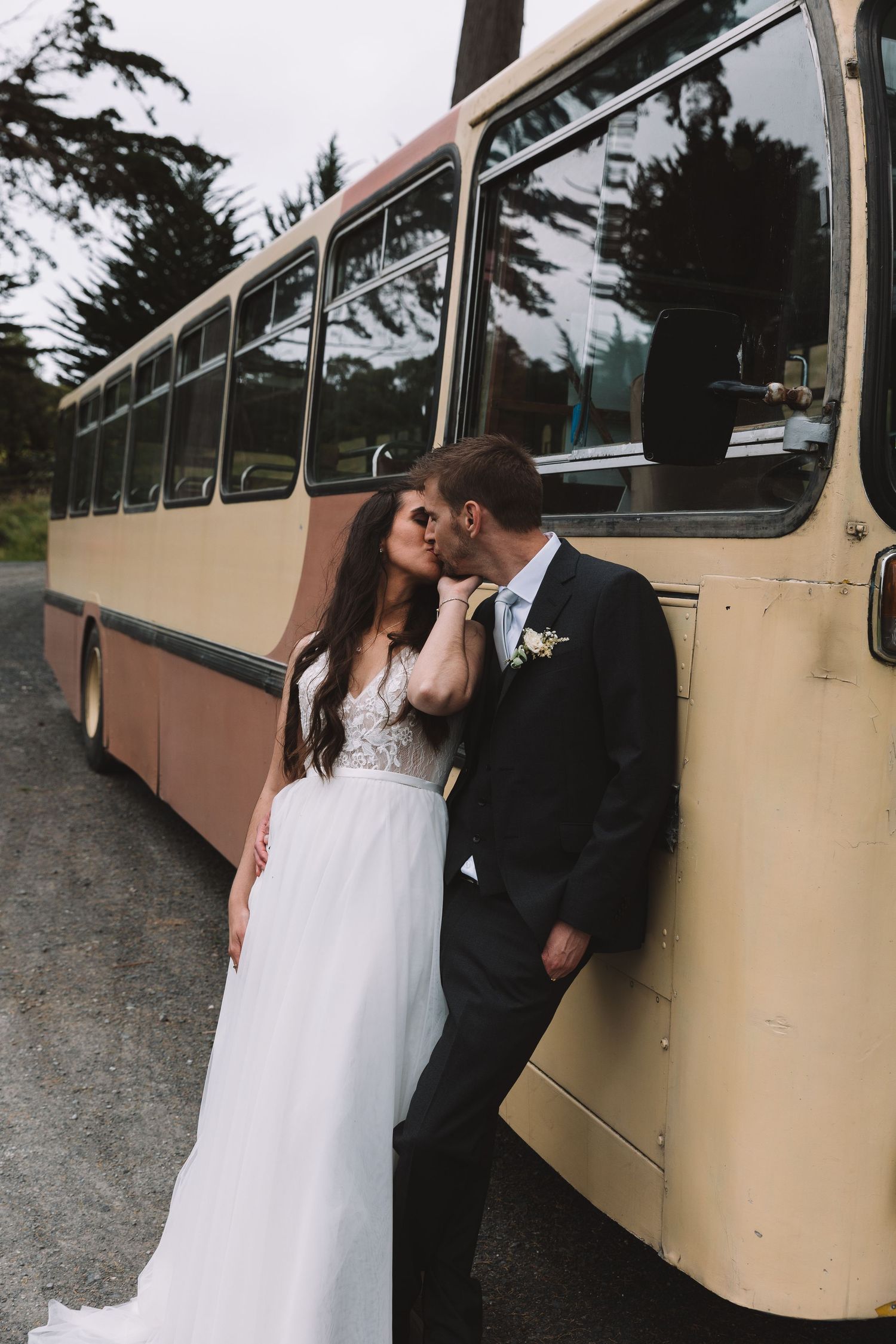A romantic wedding couple shares an intimate moment against a vintage cream-colored bus.