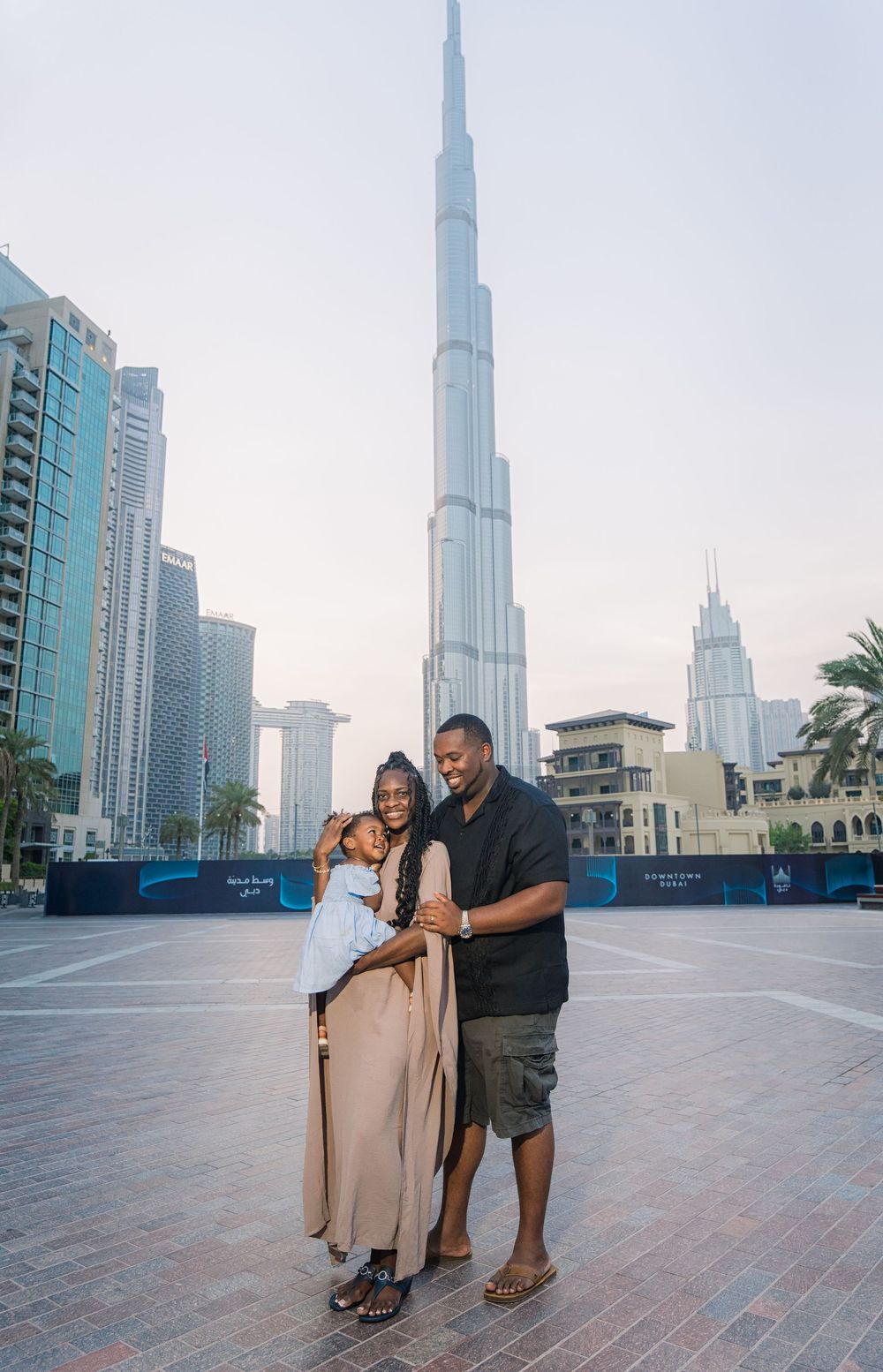 Tourists posing in front of the iconic Burj Khalifa skyscraper in downtown Dubai on a cloudy day.