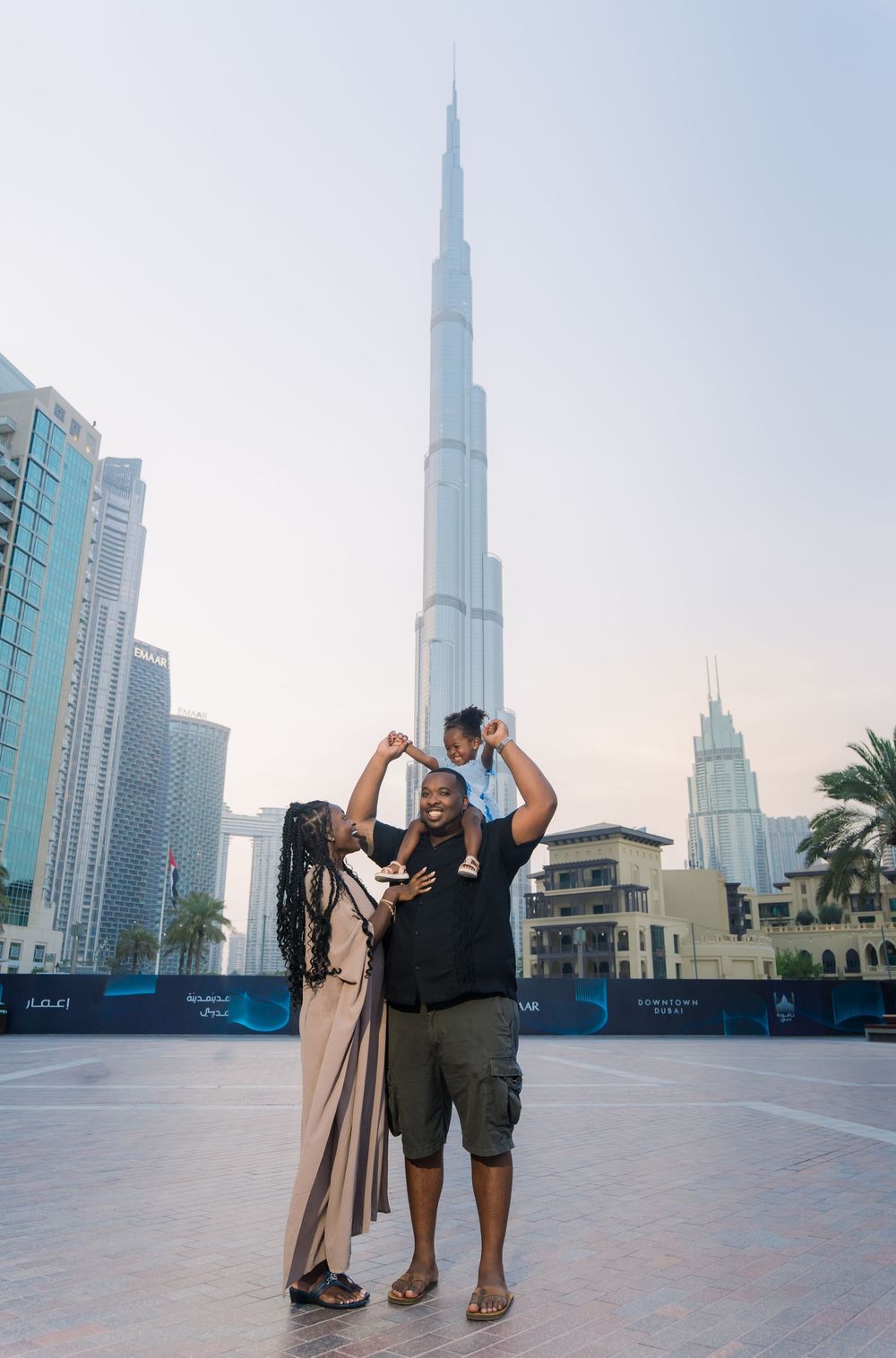 A couple stands pointing at the iconic Burj Khalifa tower in downtown Dubai during daytime.