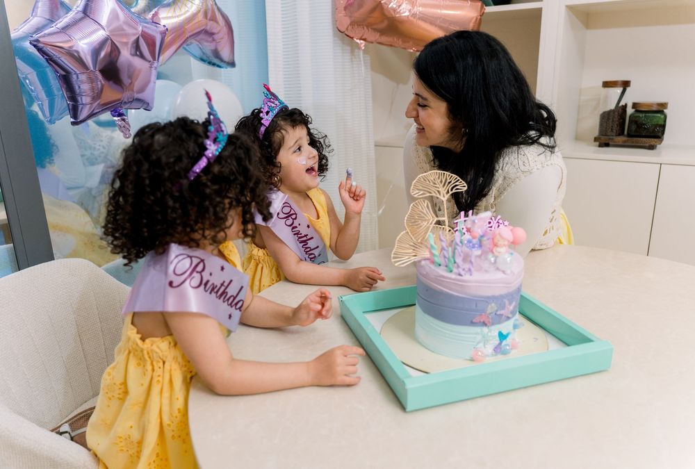 Parent and child in party outfits celebrating with a blue and purple birthday cake at home.