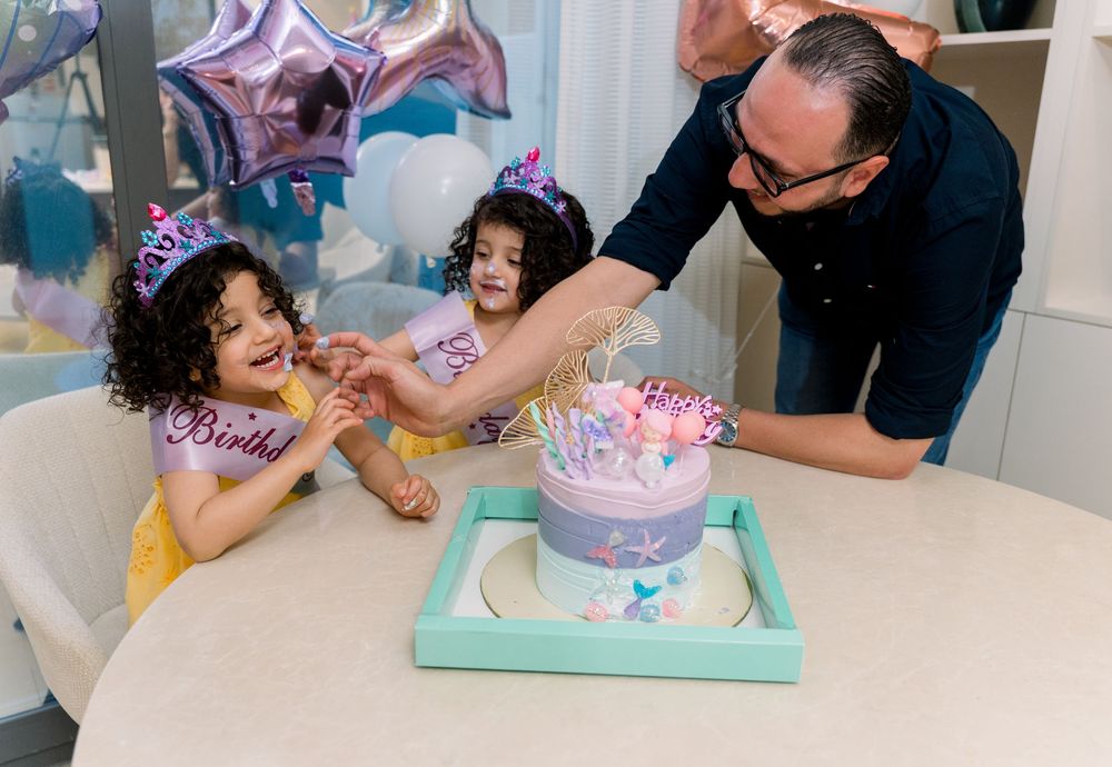 Birthday celebration scene with decorative cake on turquoise tray and pink and purple party decor in the background.