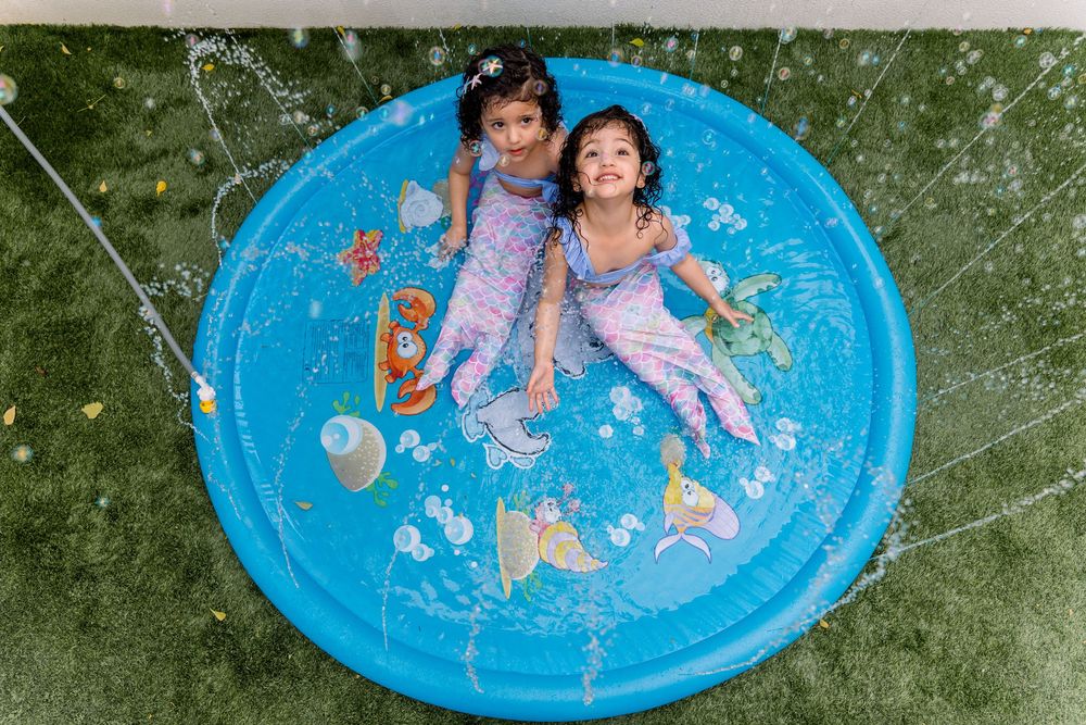Two children having fun while cooling off in a bright blue splash pad on a summer day.