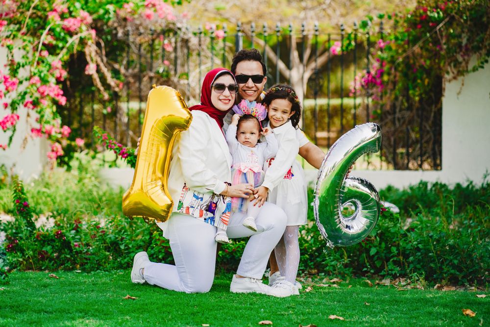 Family portrait in garden with colorful number balloons and white outfits.
