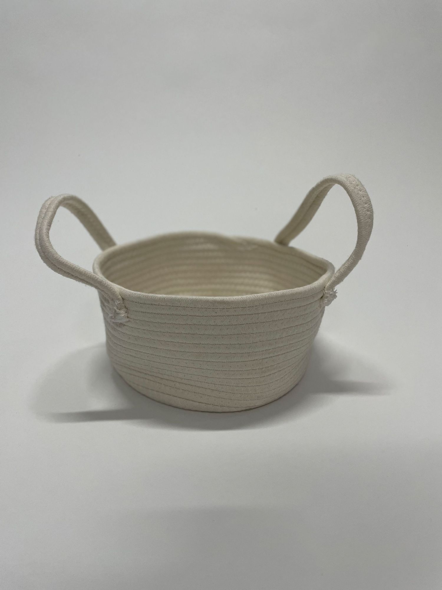 A handcrafted cotton rope bowl with handles in neutral beige color.