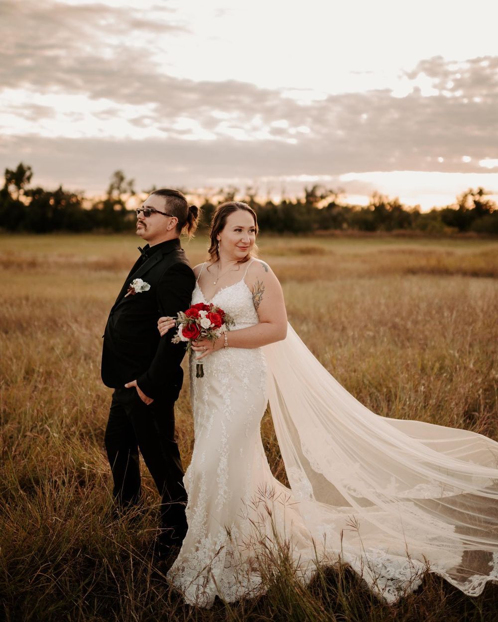 Wedding couple dances joyfully in field as bride's dress flows in evening breeze. Oklahoma Wedding Photographer
