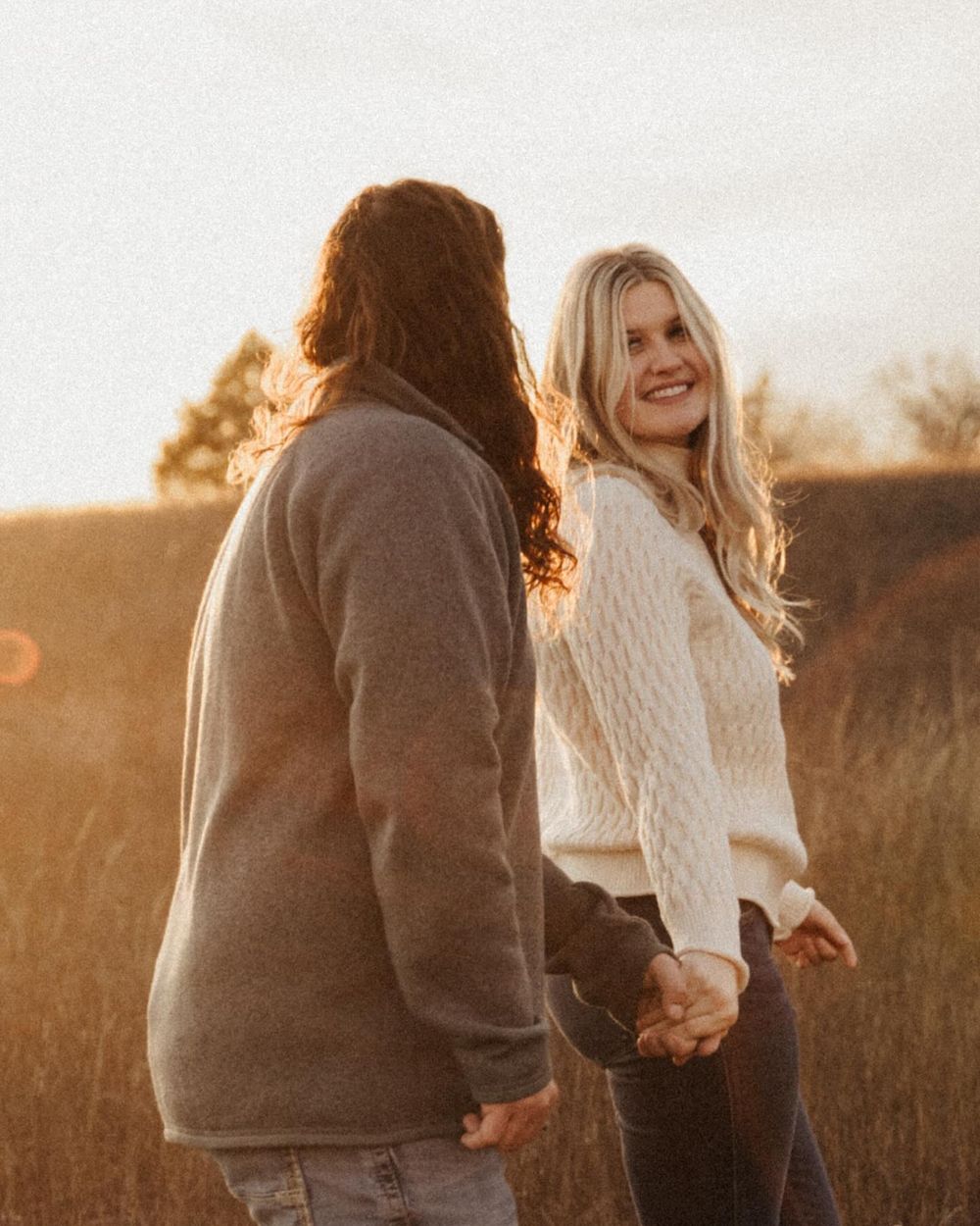 A couple sharing laughter during a sunset engagement session in a golden field. Oklahoma Wedding Photographer