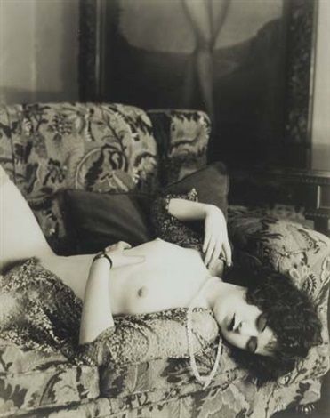 Black and white glamour photo of a figure reclining on a patterned sofa in vintage attire.