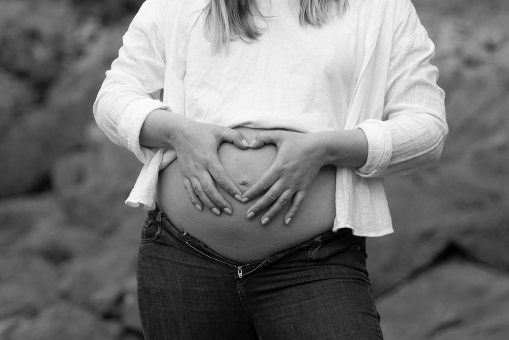 Black and white close-up of hands forming heart shape on pregnant belly.