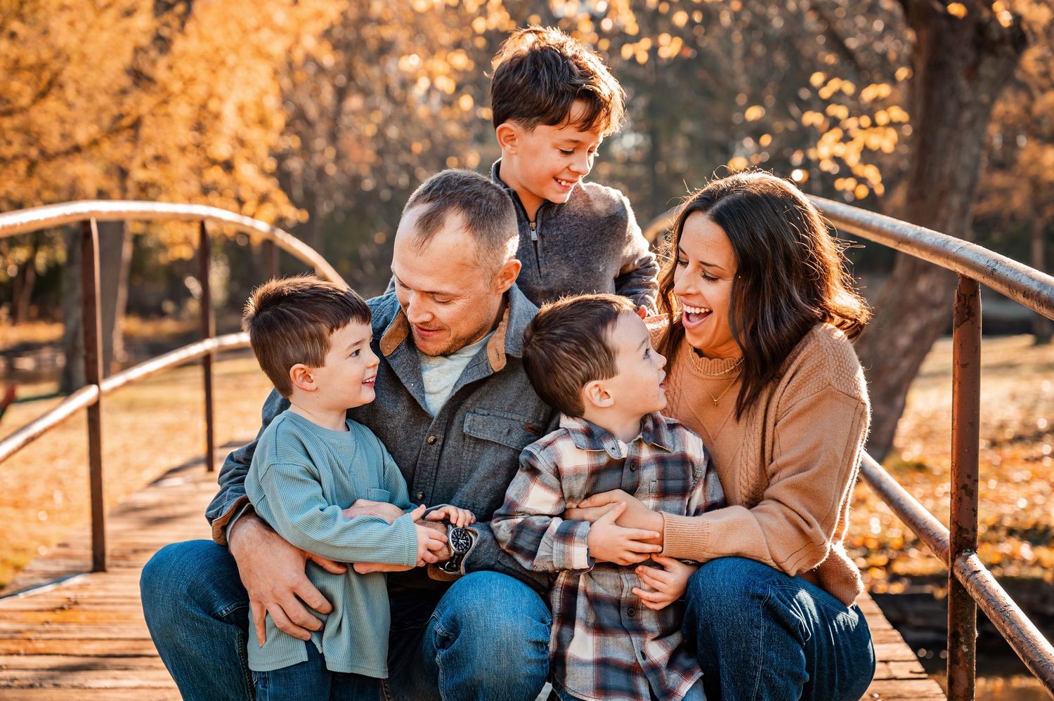 A loving family shares a joyful moment together on a bridge during golden hour in an autumn setting.