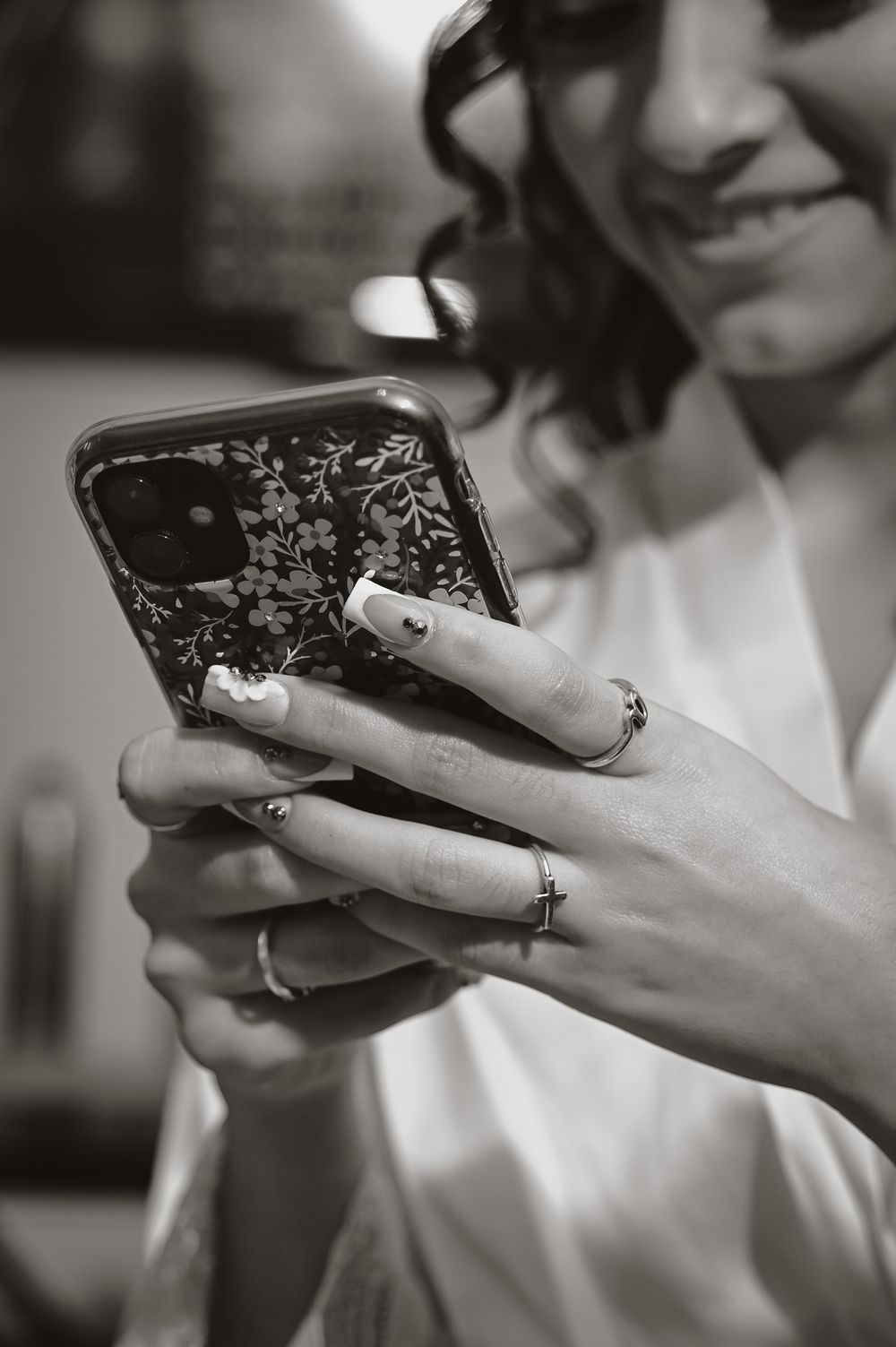Hands holding a floral phone case while wearing delicate rings.