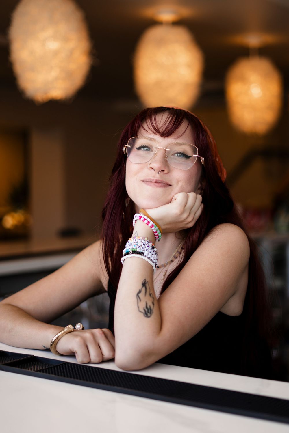 Person with red hair and glasses rests head on hand at counter with warm lighting.